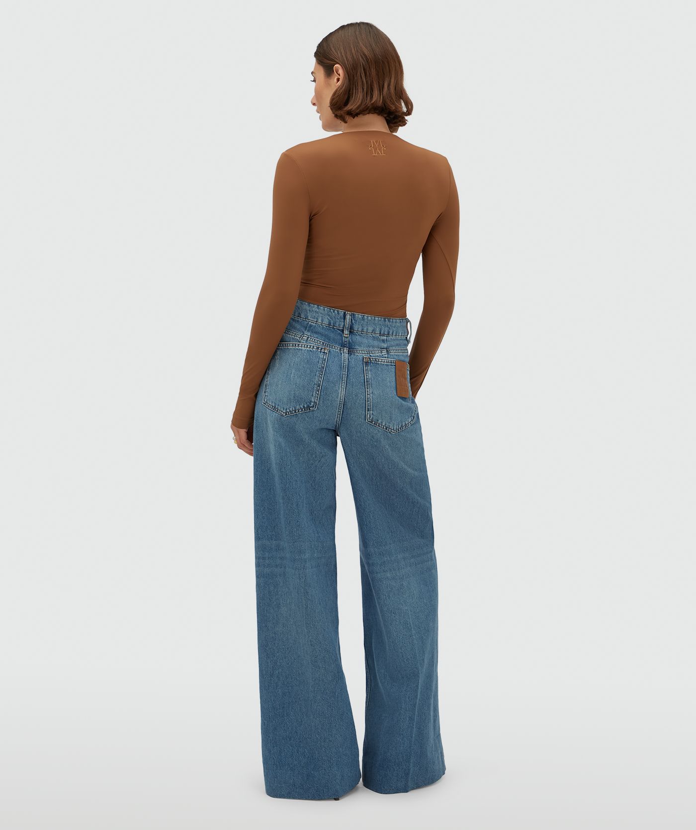 Model draagt een jeans met leren details aan de bovenkant, gecombineerd met een cognackleurige top.