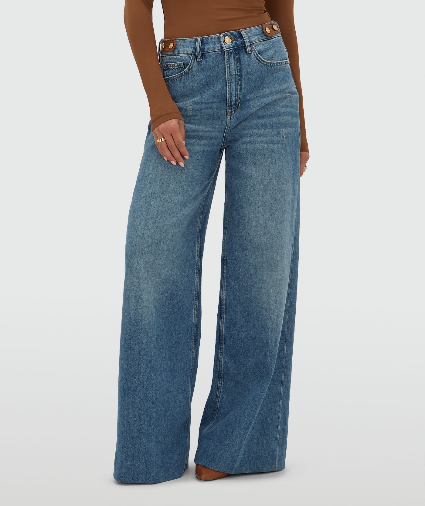 Model draagt een jeans met leren details aan de bovenkant, gecombineerd met een cognackleurige top.