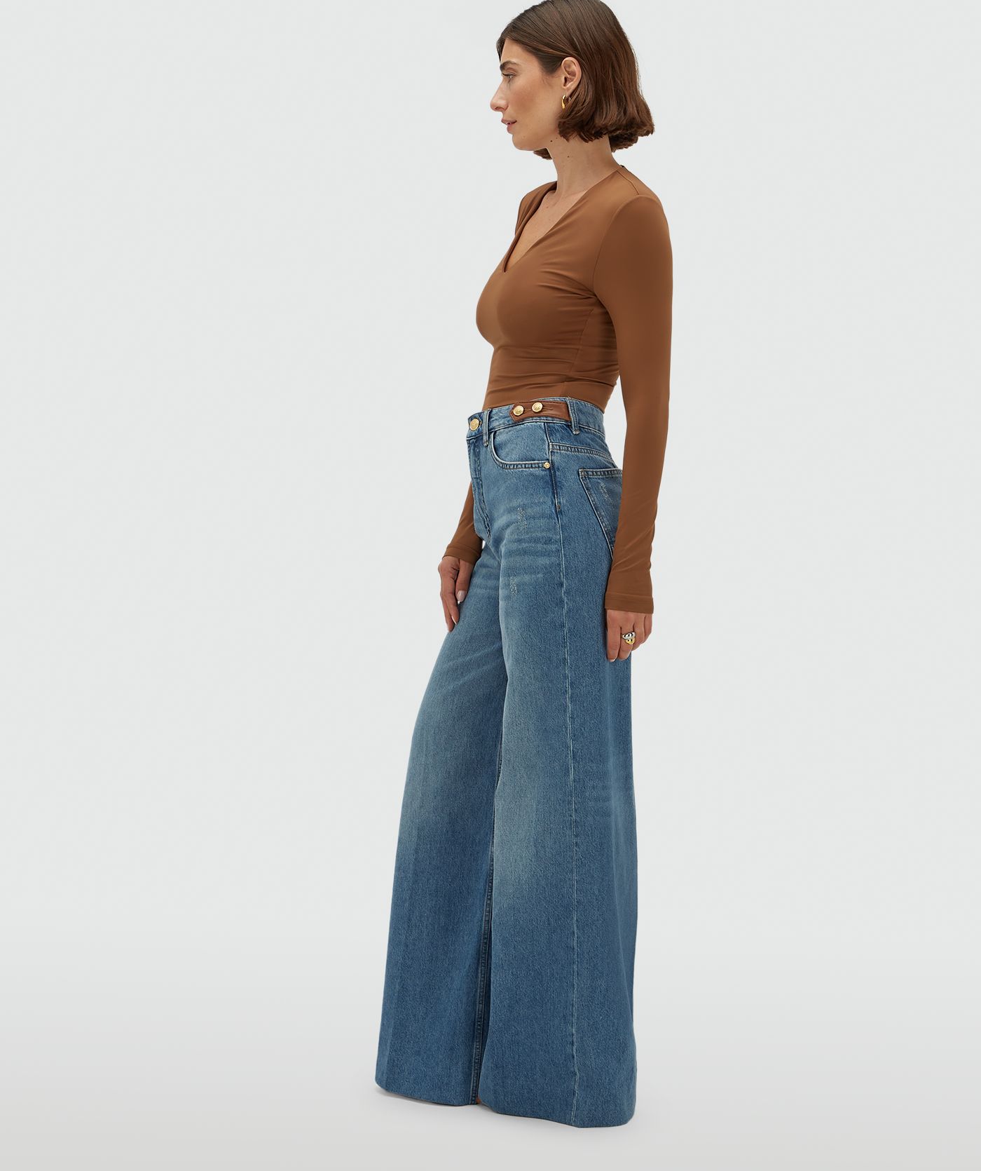 Model draagt een jeans met leren details aan de bovenkant, gecombineerd met een cognackleurige top.