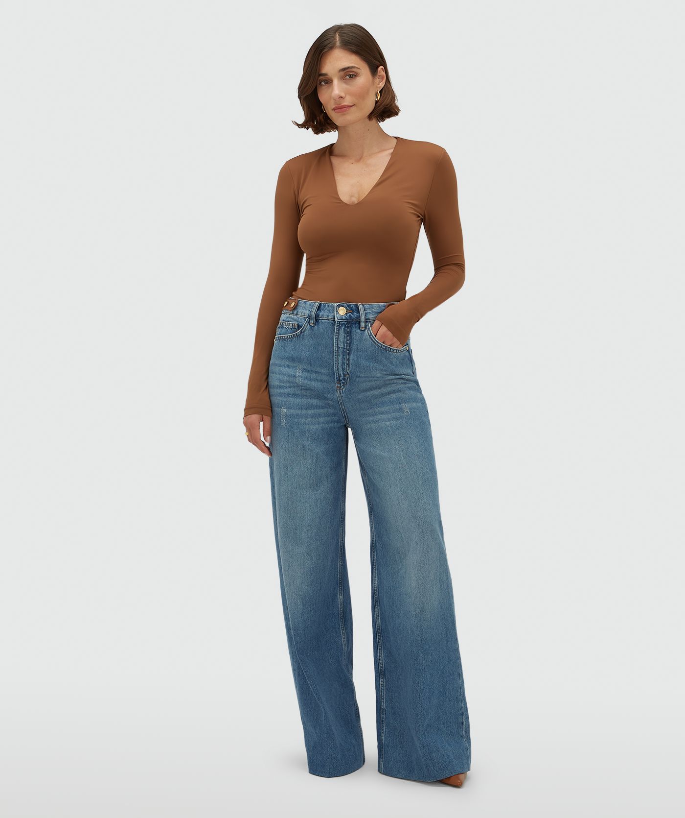 Model draagt een jeans met leren details aan de bovenkant, gecombineerd met een cognackleurige top.