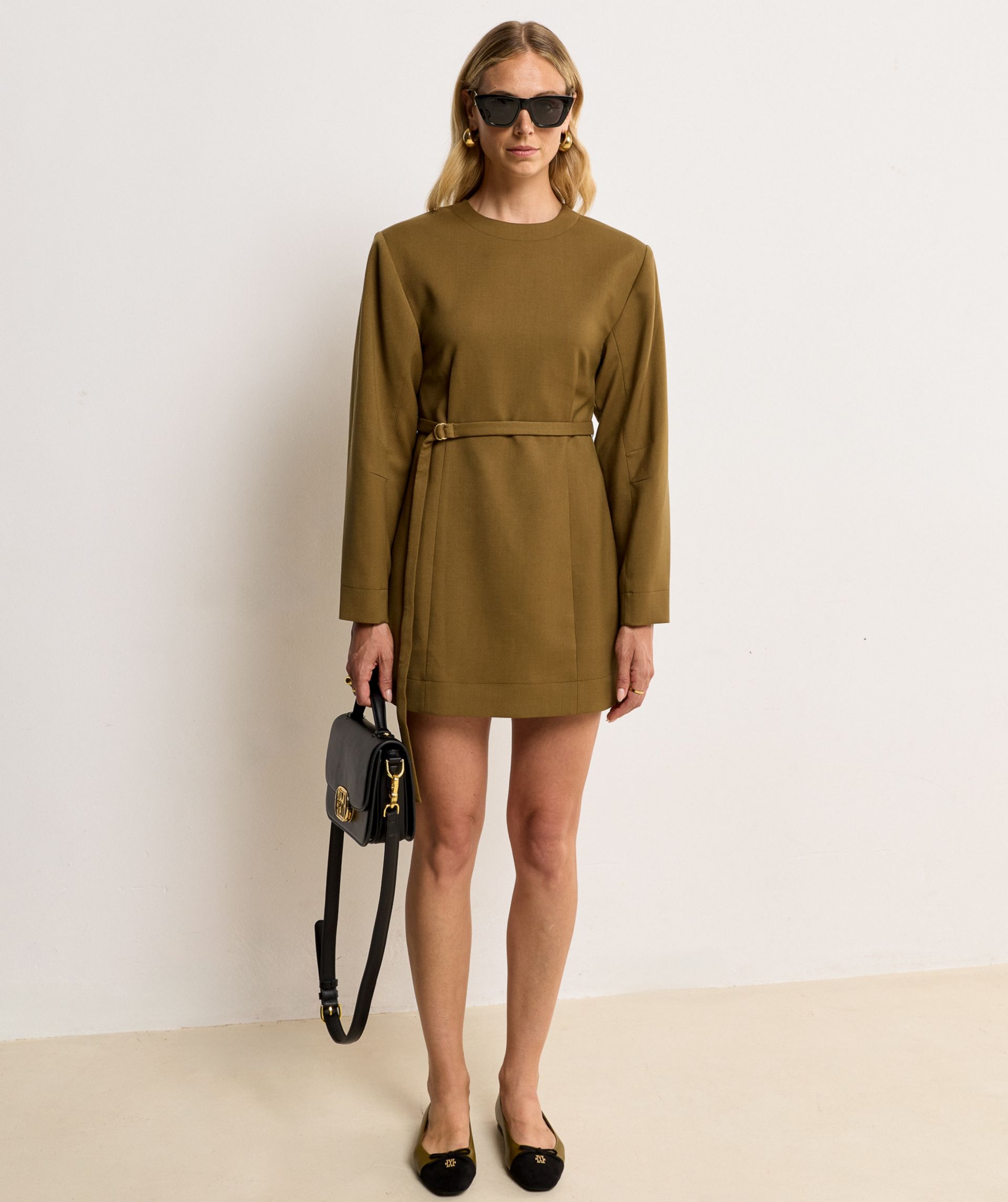 Model draagt Olive Green ballerinas met een zwarte suede neus, een strikdetail en een goudkleurig logo