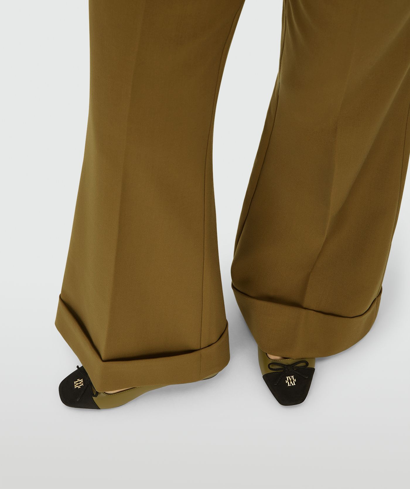 Model draagt Olive Green ballerinas met een zwarte suede neus, een strikdetail en een goudkleurig logo