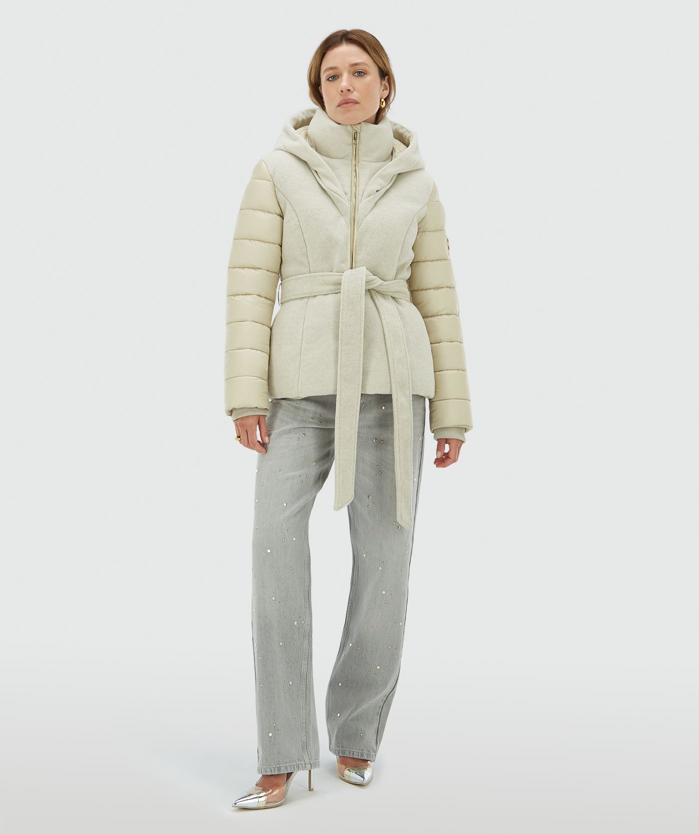 Model draagt een light beige gewatteerde jas met capuchon, hoge kraag en ceintuur - Josh V