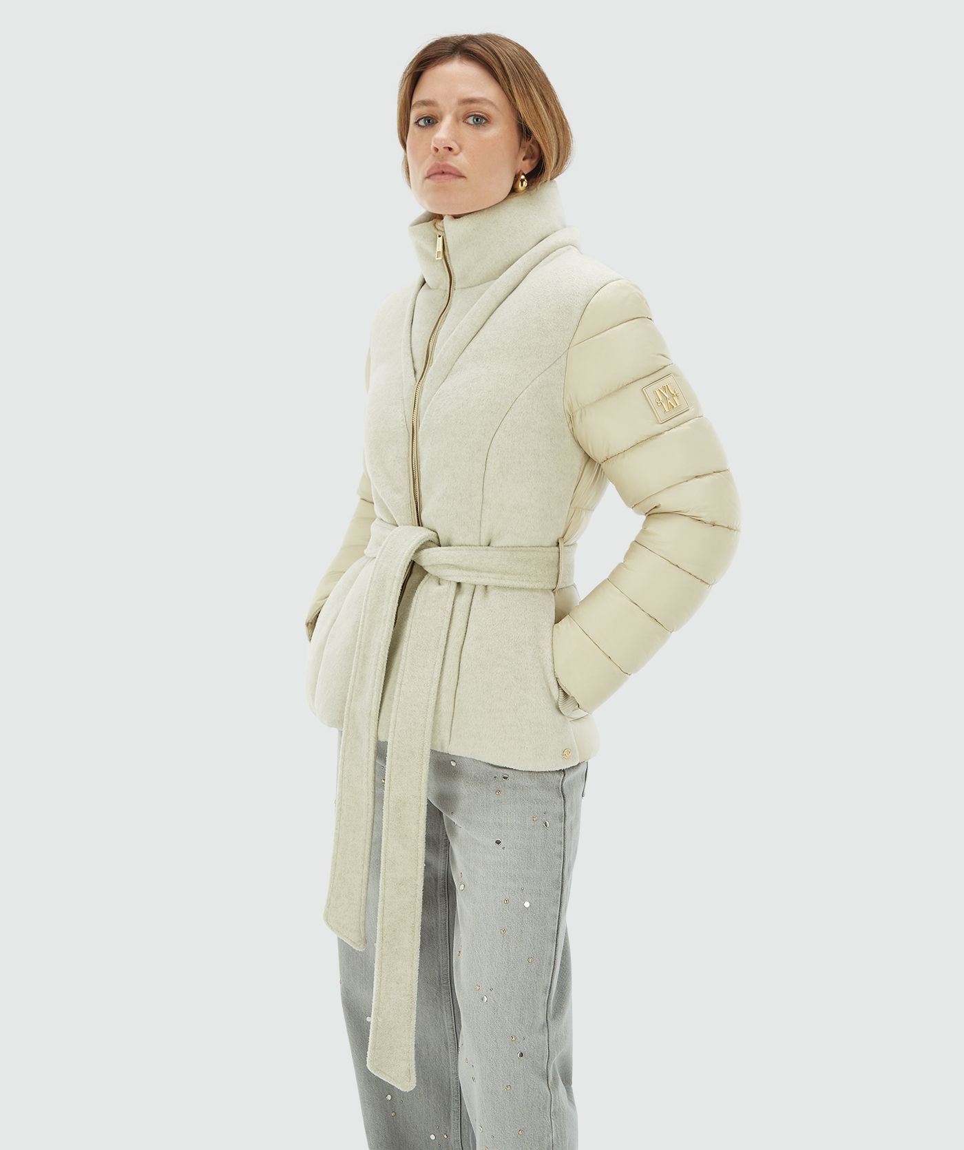 Model draagt een light beige gewatteerde jas met capuchon, hoge kraag en ceintuur - Josh V