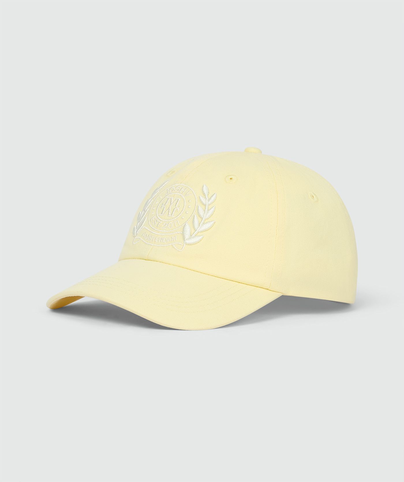 Pet in de kleur Butter Yellow met geborduurde logo op de voorkant, weergegeven op een lichtgrijze achtergrond