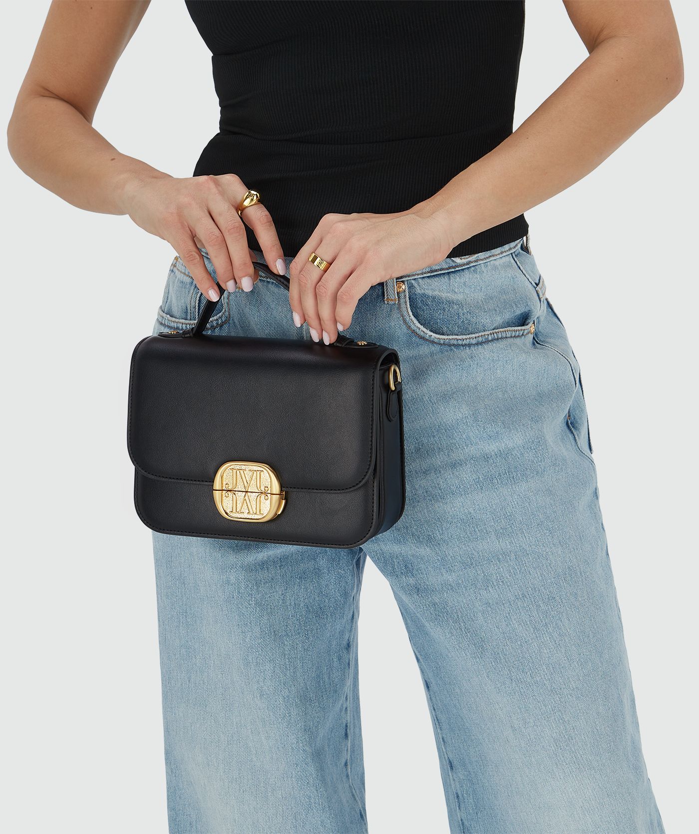 Het model houdt een tas in het zwart met een goudkleurige bucklesluiting vast aan het handhengsel