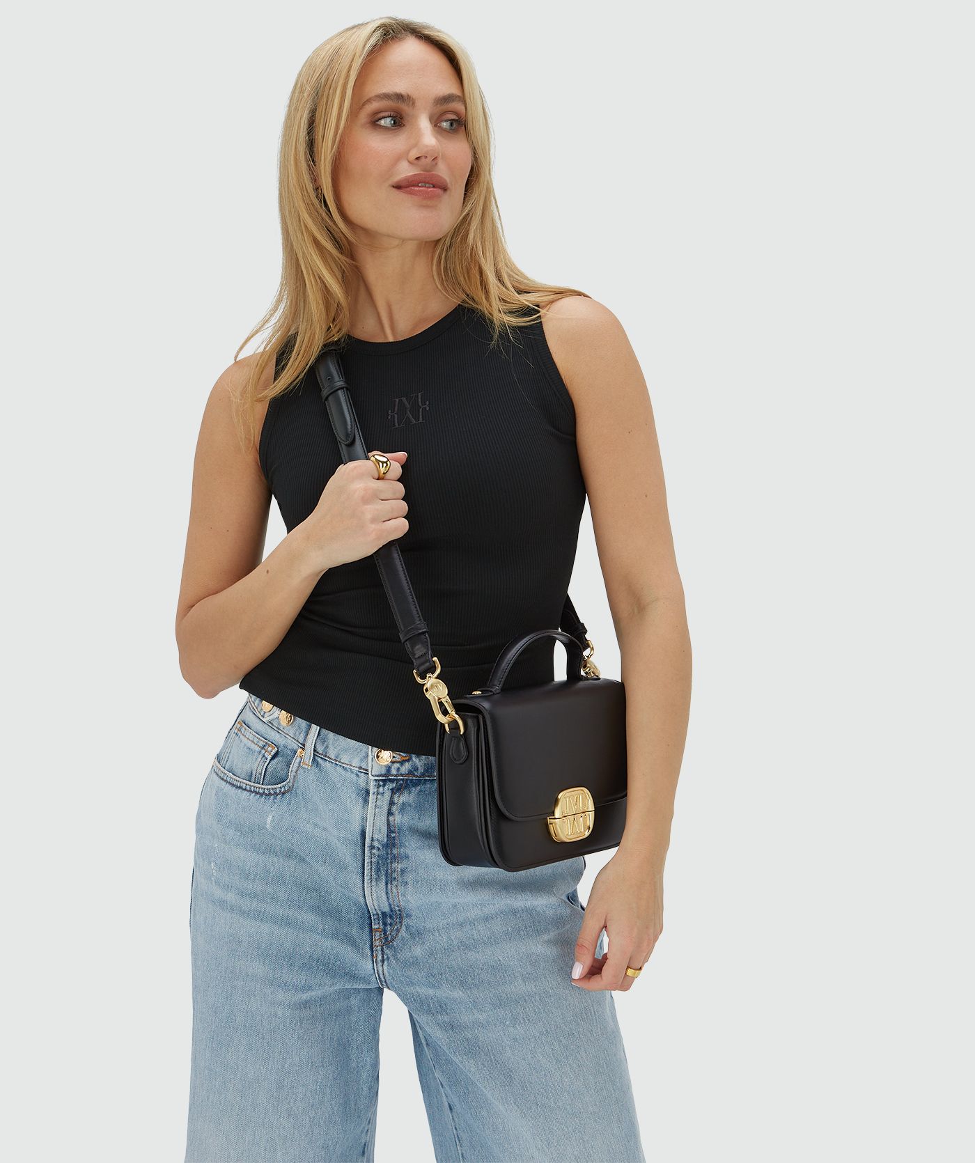 Het model draagt een tas in het zwart met een goudkleurige bucklesluiting crossbody