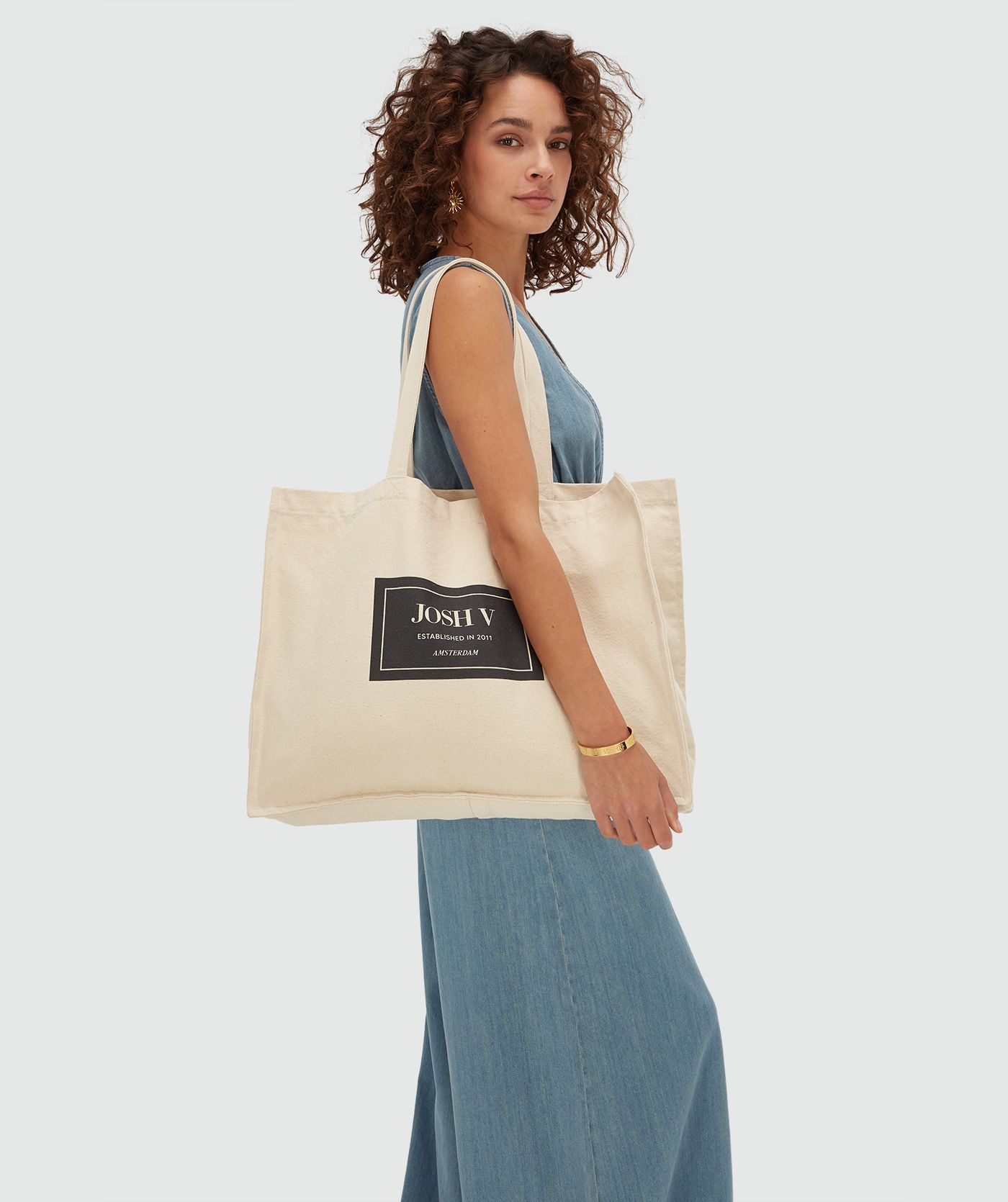 Model heeft de 15 YEARS canvas tas met zwart JV embleem over haar rechter schouder