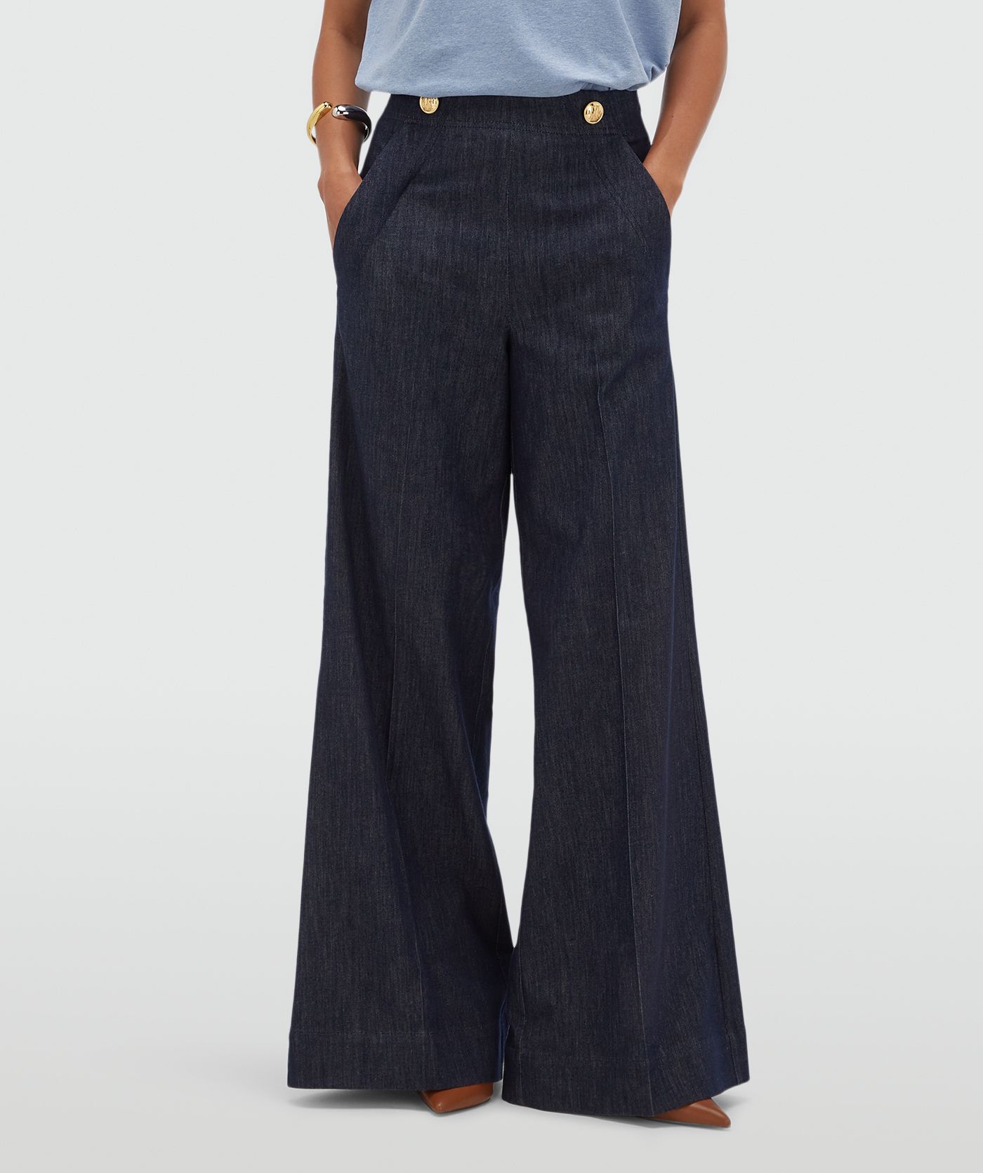 Model draagt een donkerblauwe wide leg pantalon met gouden knopen aan de bovenkant.