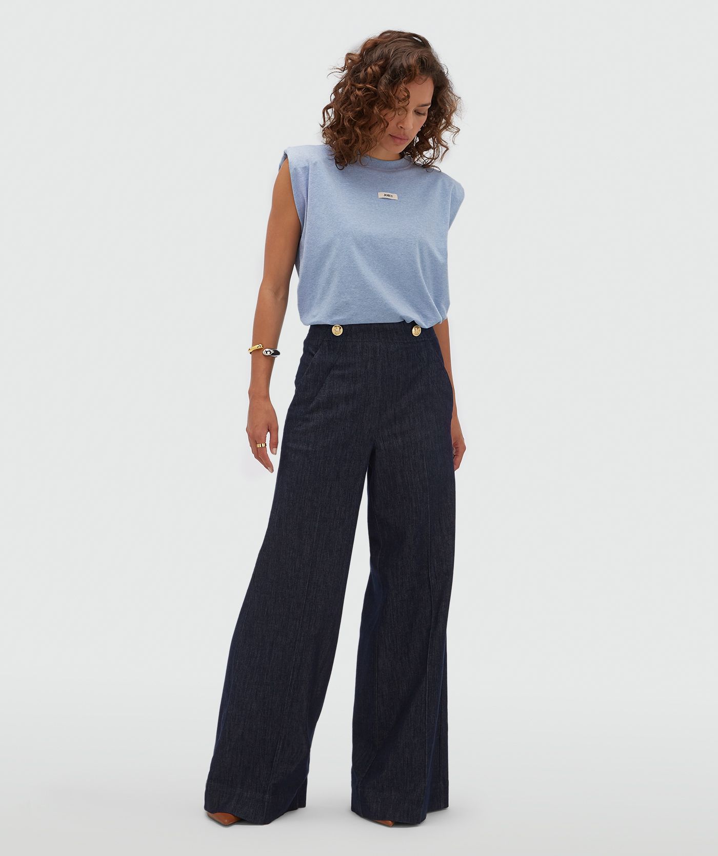 Model draagt een donkerblauwe wide leg pantalon met gouden knopen aan de bovenkant.