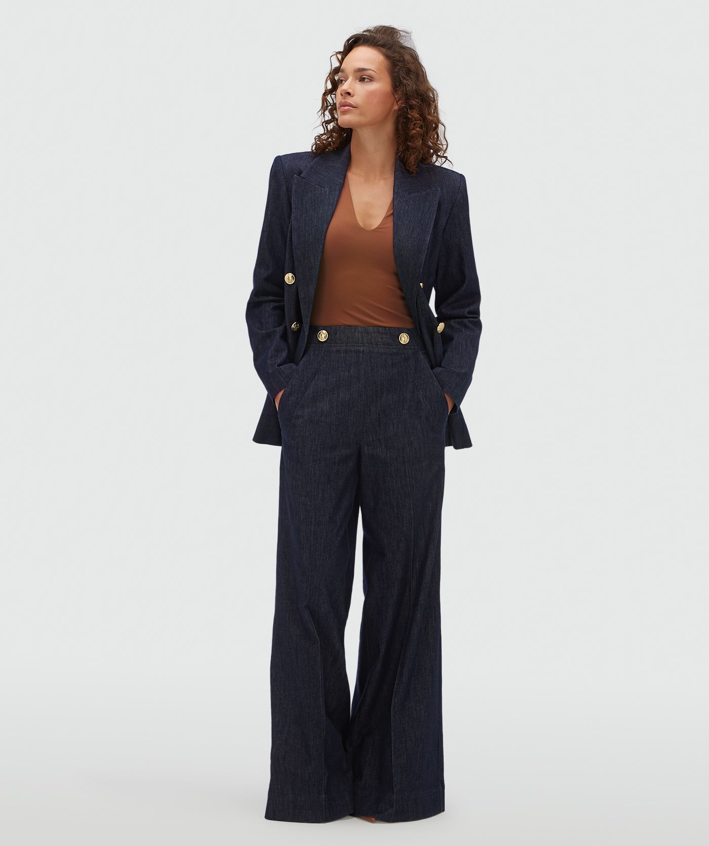 Model draagt een donkerblauwe wide leg pantalon met gouden knopen aan de bovenkant.