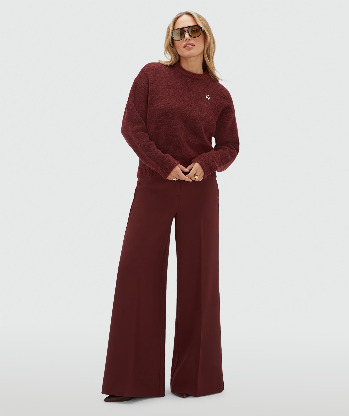Model draagt een donkerrode trui met een klein gouden JOSH V logo gecombineerd met een donkerrode pantalon.