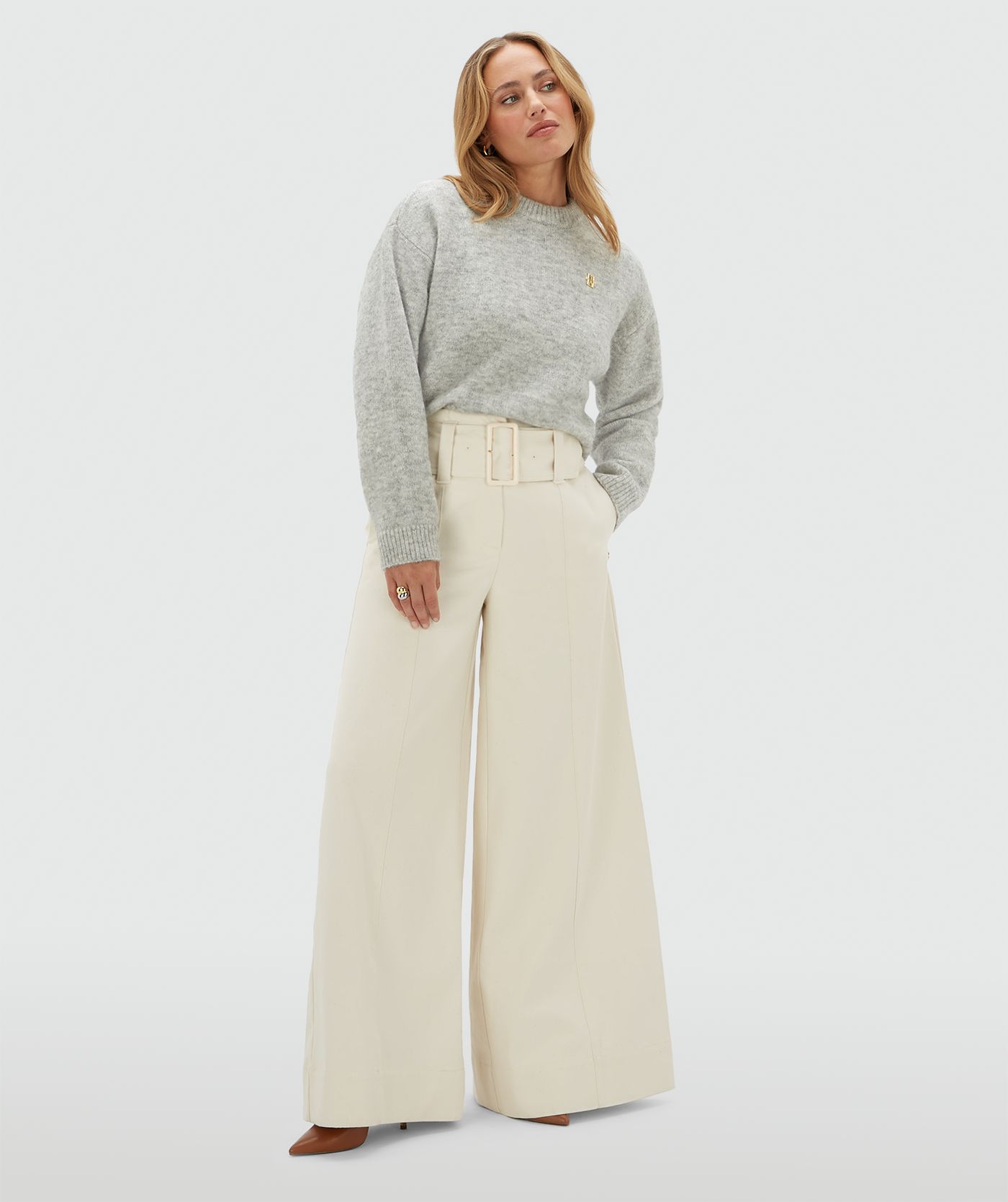 Model draagt een lichtgrijze sweater met een klein JOSH V logo op de borst en is gecombineerd met een gebroken witte broek.