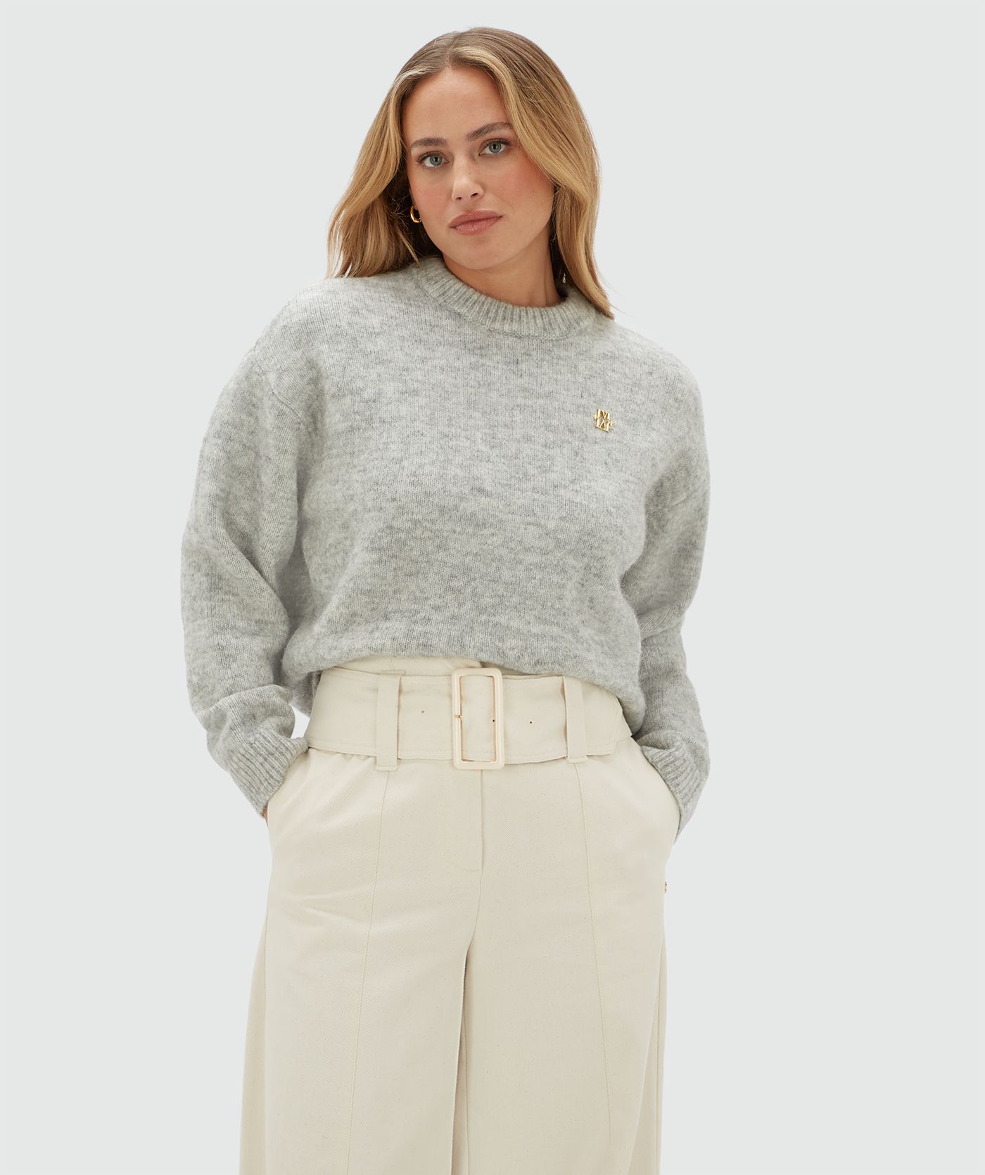 Model draagt een lichtgrijze sweater met een klein JOSH V logo op de borst en is gecombineerd met een gebroken witte broek.