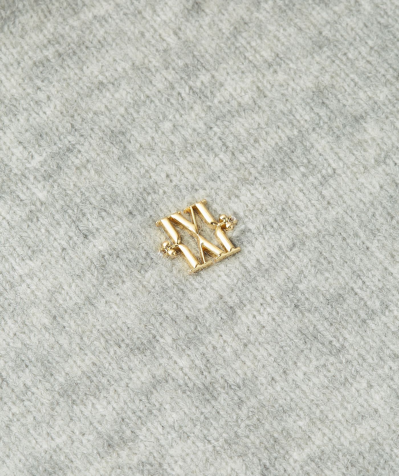 Close-up van gouden JSOH V logo op de borst van de lichtgrijze trui.