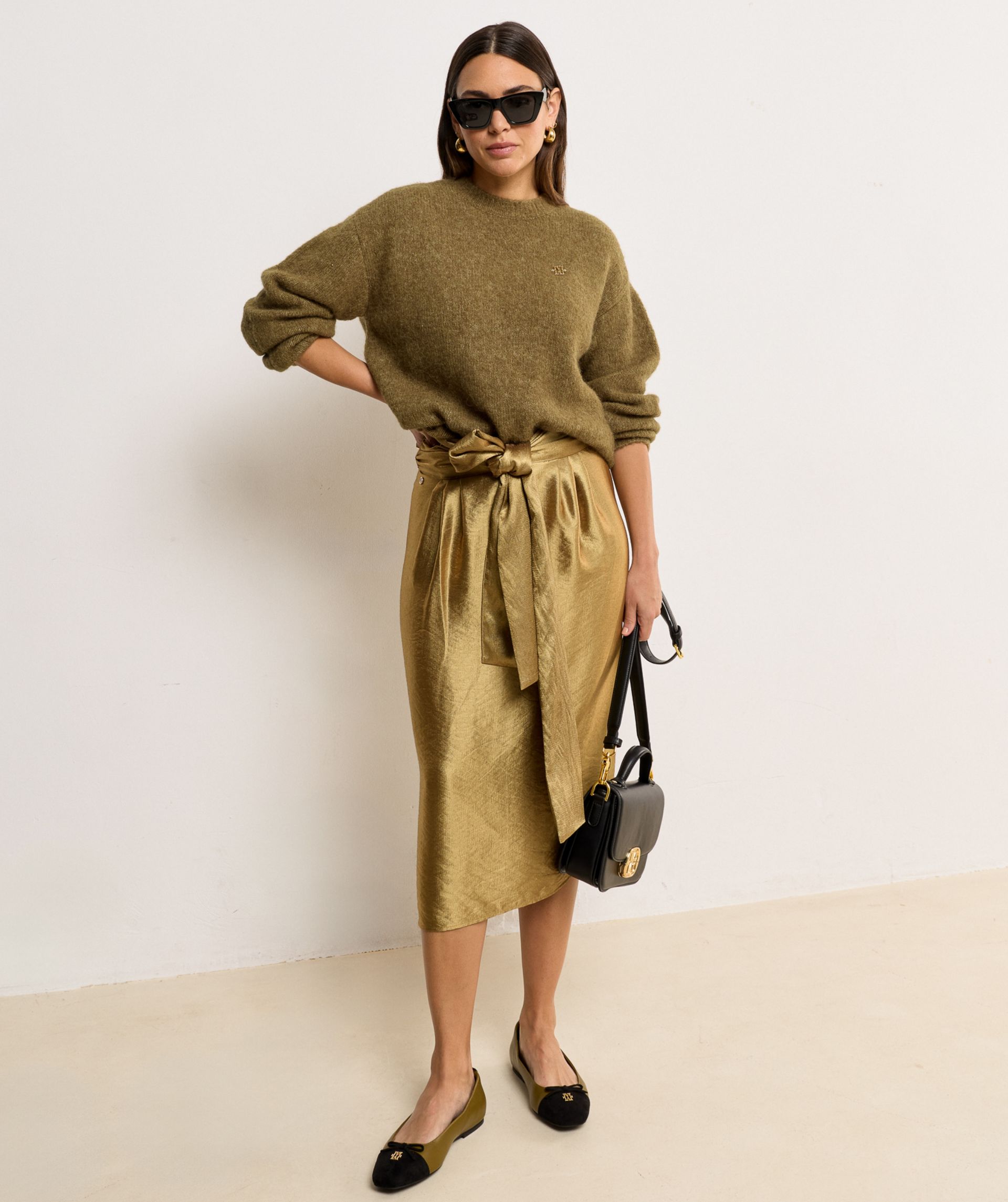 Model draagt een Dark Gold midi kort met een overslagdetail en een strikceintuur in de taille