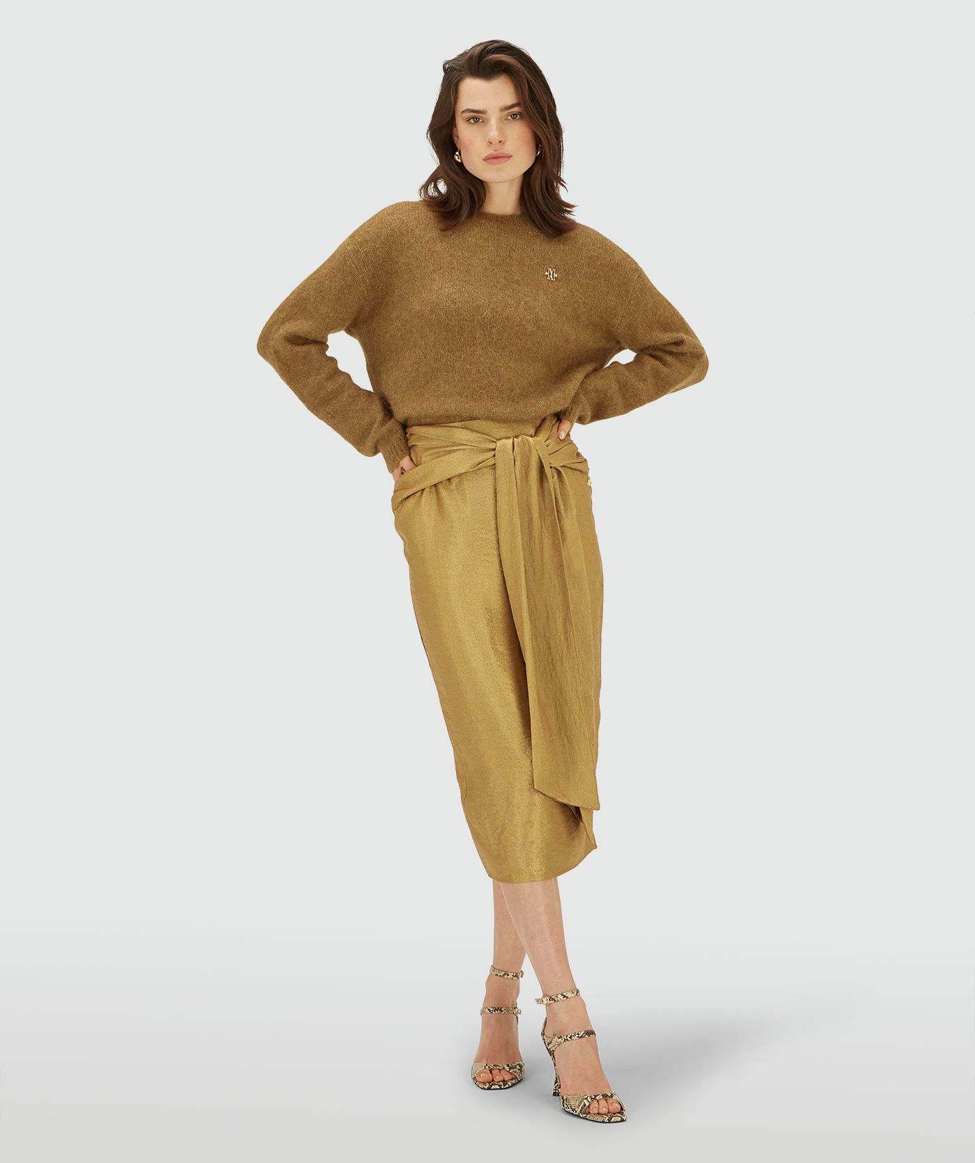 Model draagt een Dark Gold midi kort met een overslagdetail en een strikceintuur in de taille