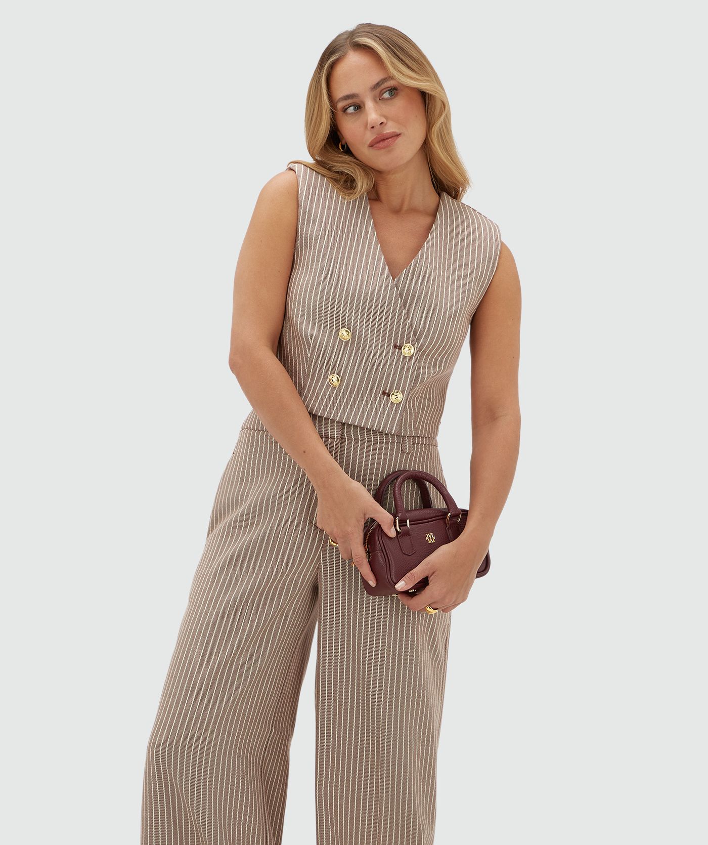 Model draagt een donkerrood wit gestreept gilet met gouden knopen gecombineerd met de bijpassende pantalon en een donkerrood tasje.