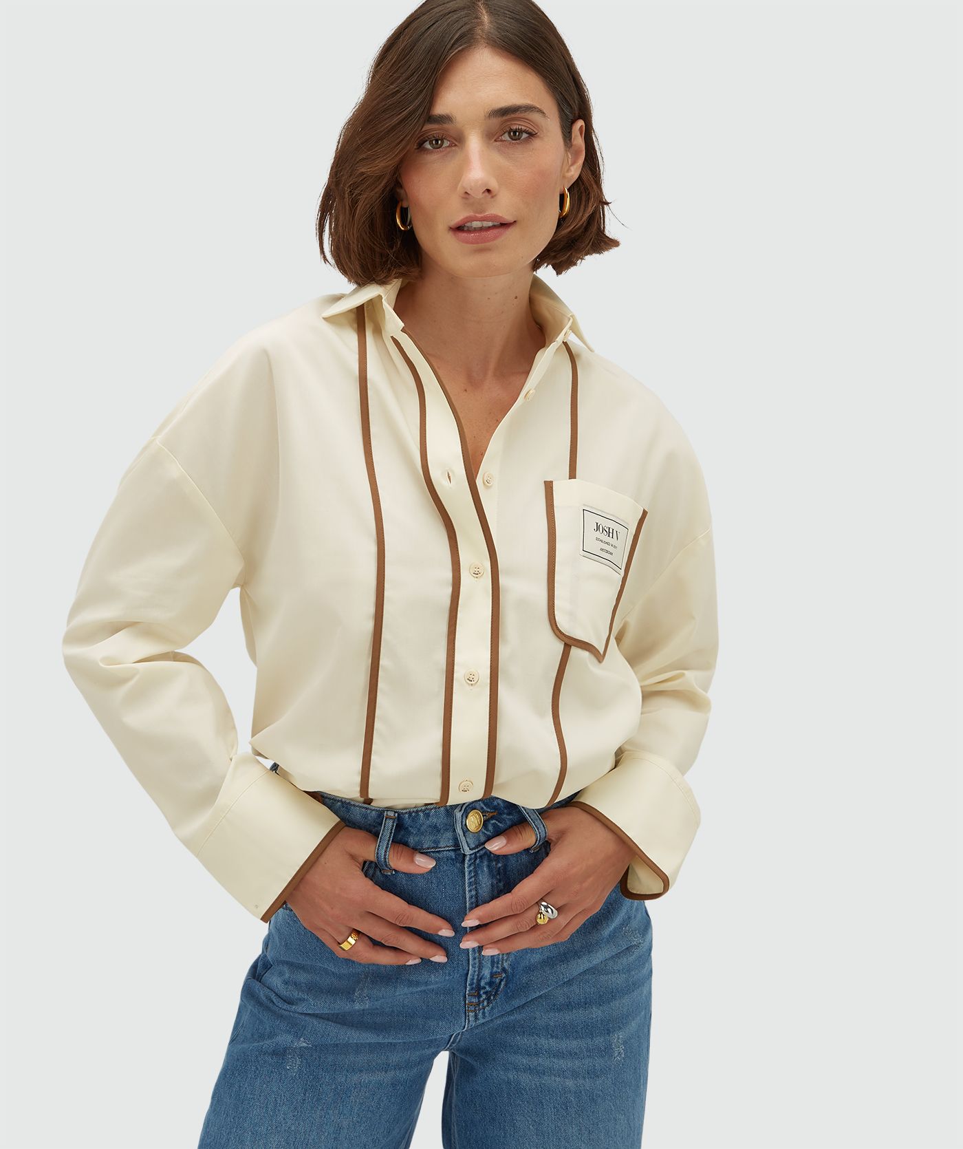 Model draagt een oversized witte blouse met bruine details