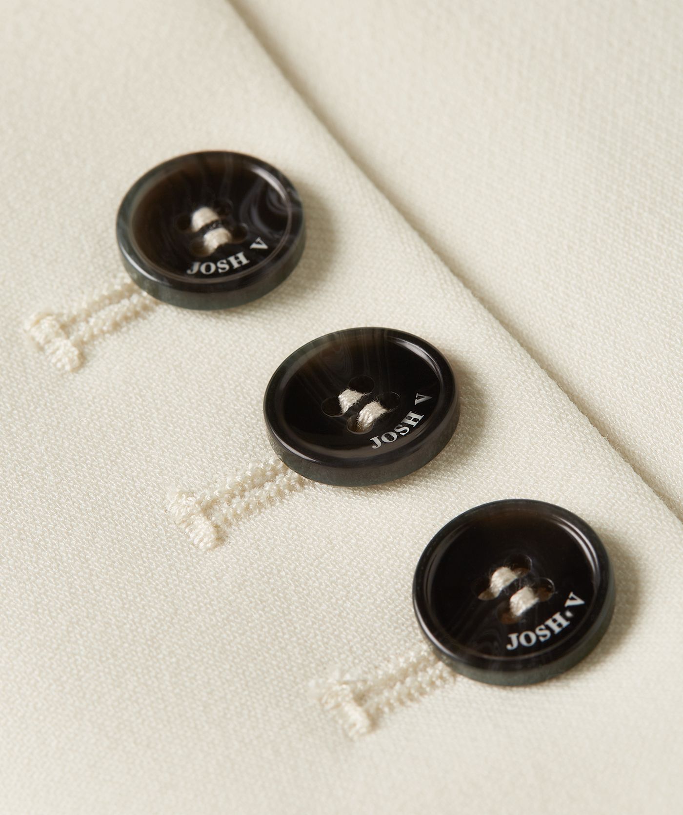 Close-up van drie zwarte knopen met het JOSH V-logo op een crème blazer - JOSH V