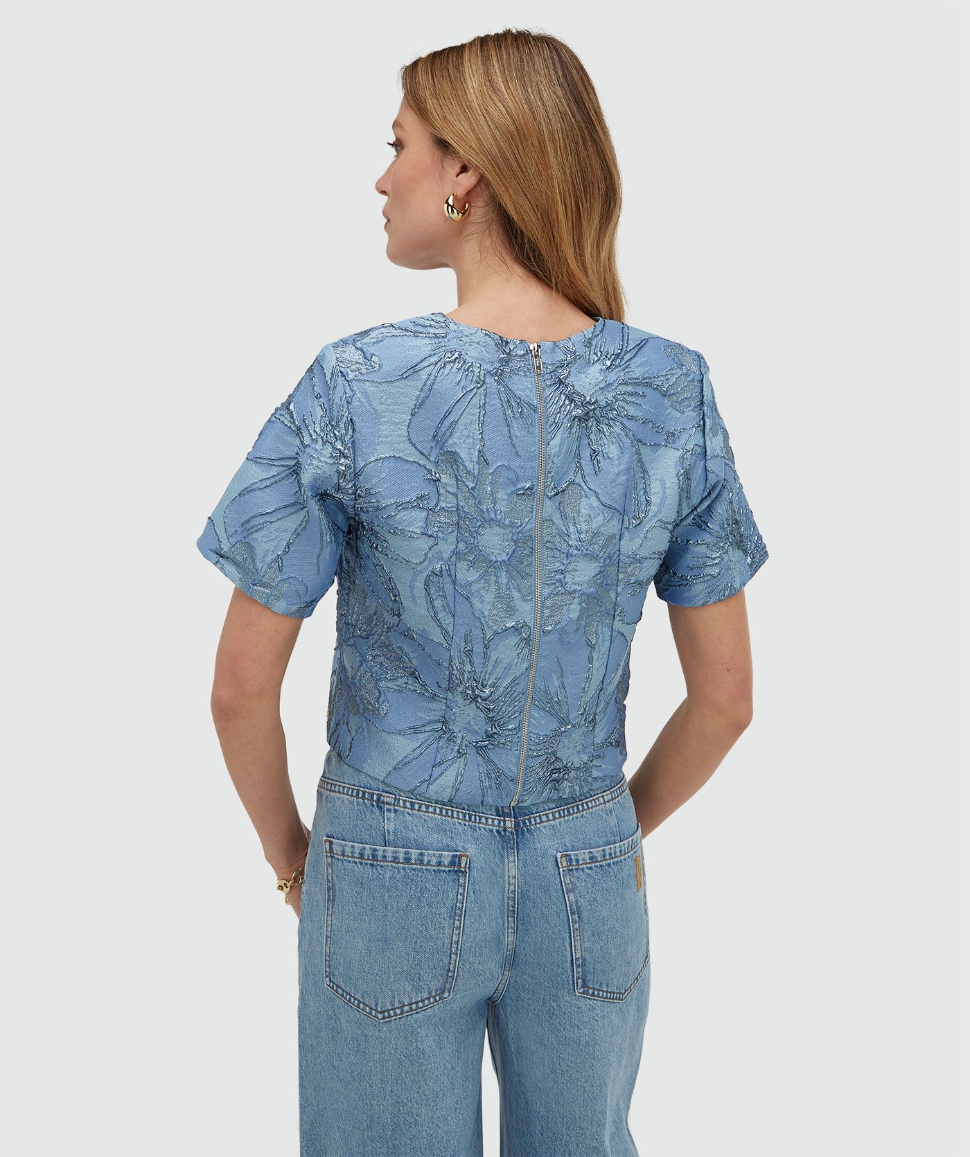 Achteraanzicht van een model in een cropped top met metallic details in de kleur Fresh Blue