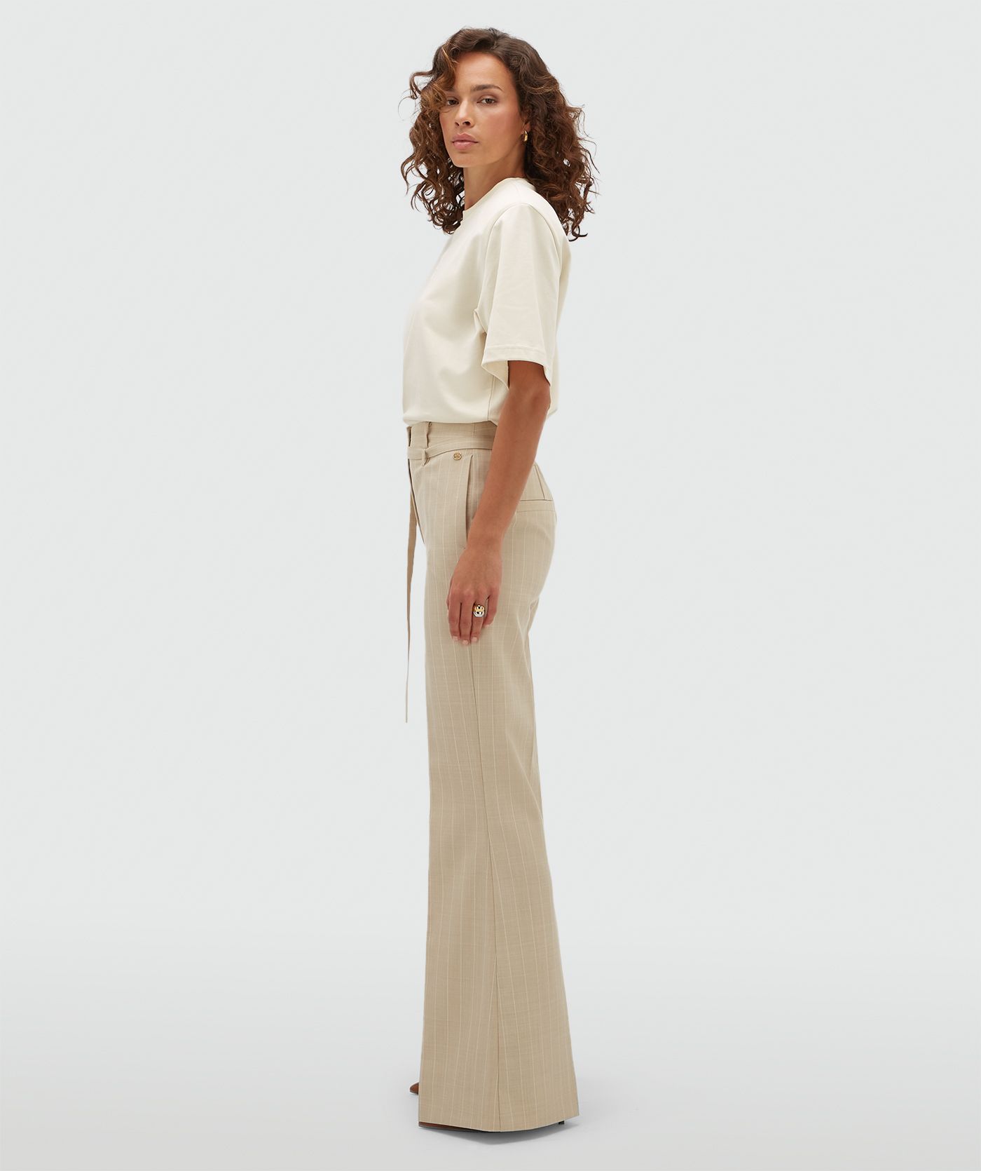 Model van opzij in een beige flared pantalon met krijtstreep.