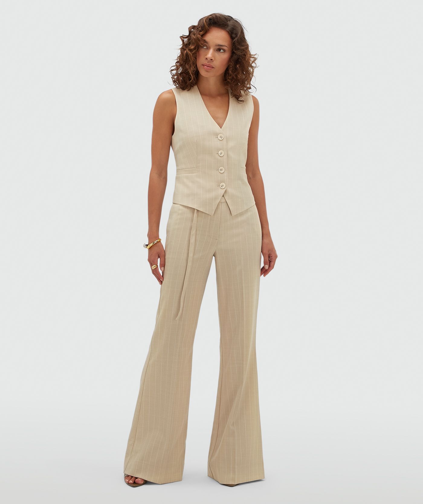 Model draagt een beige flared pantalon met krijtstreep.