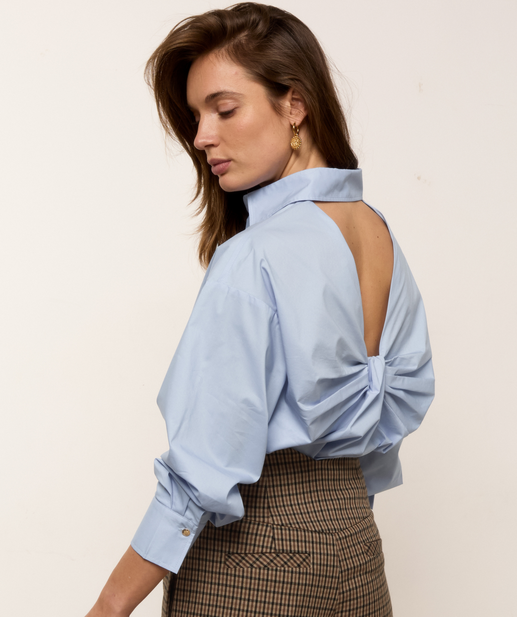 Lookbook beeld waar het model een lichtblauwe oversized blouse draagt met een strikdetail aan de achterzijde