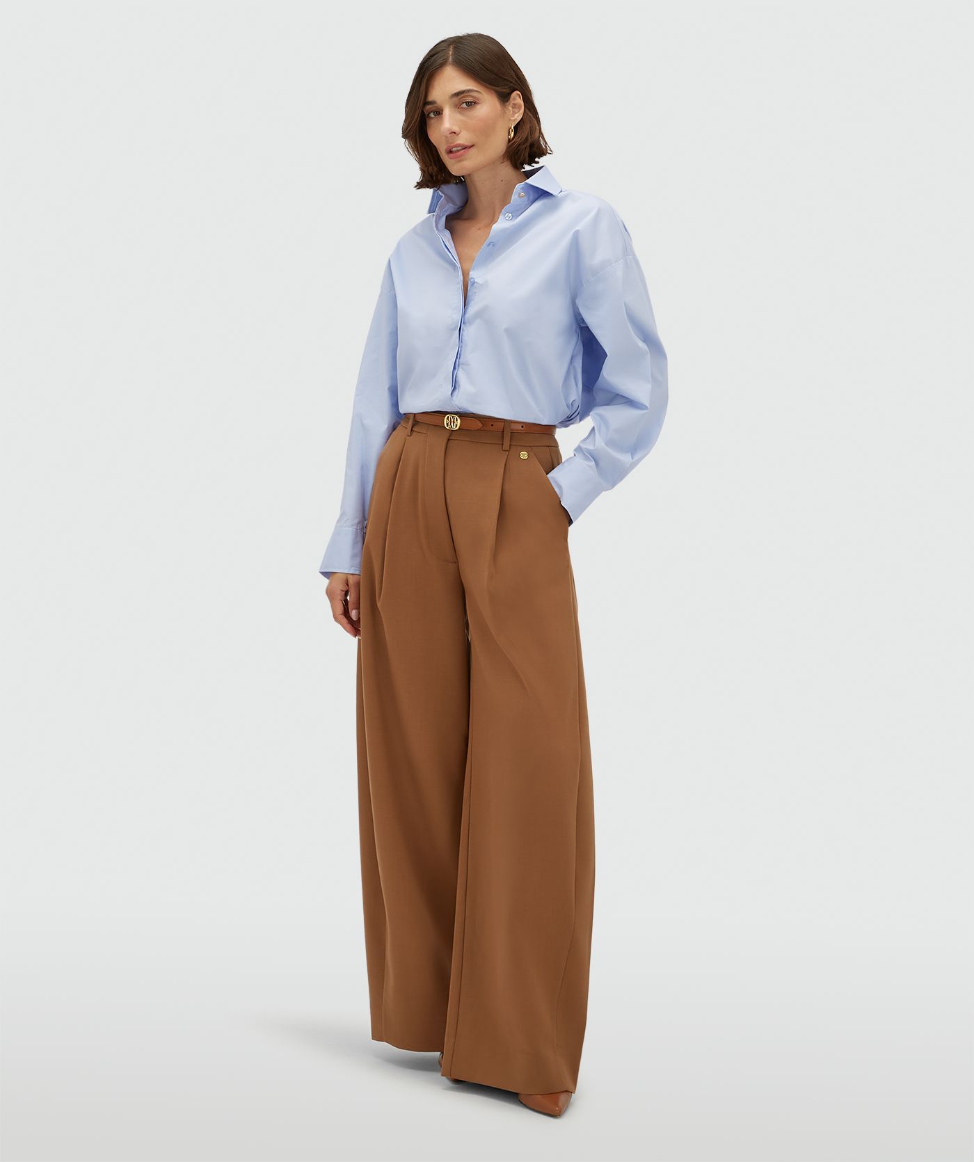 Model draagt een oversized licht blauwe blouse met strikdetail aan de achterzijde. 