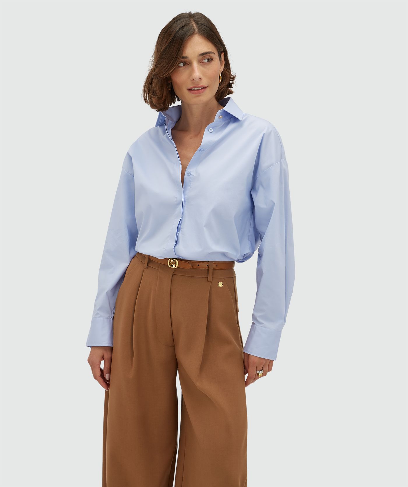 Model draagt een oversized licht blauwe blouse met strikdetail aan de achterzijde. 