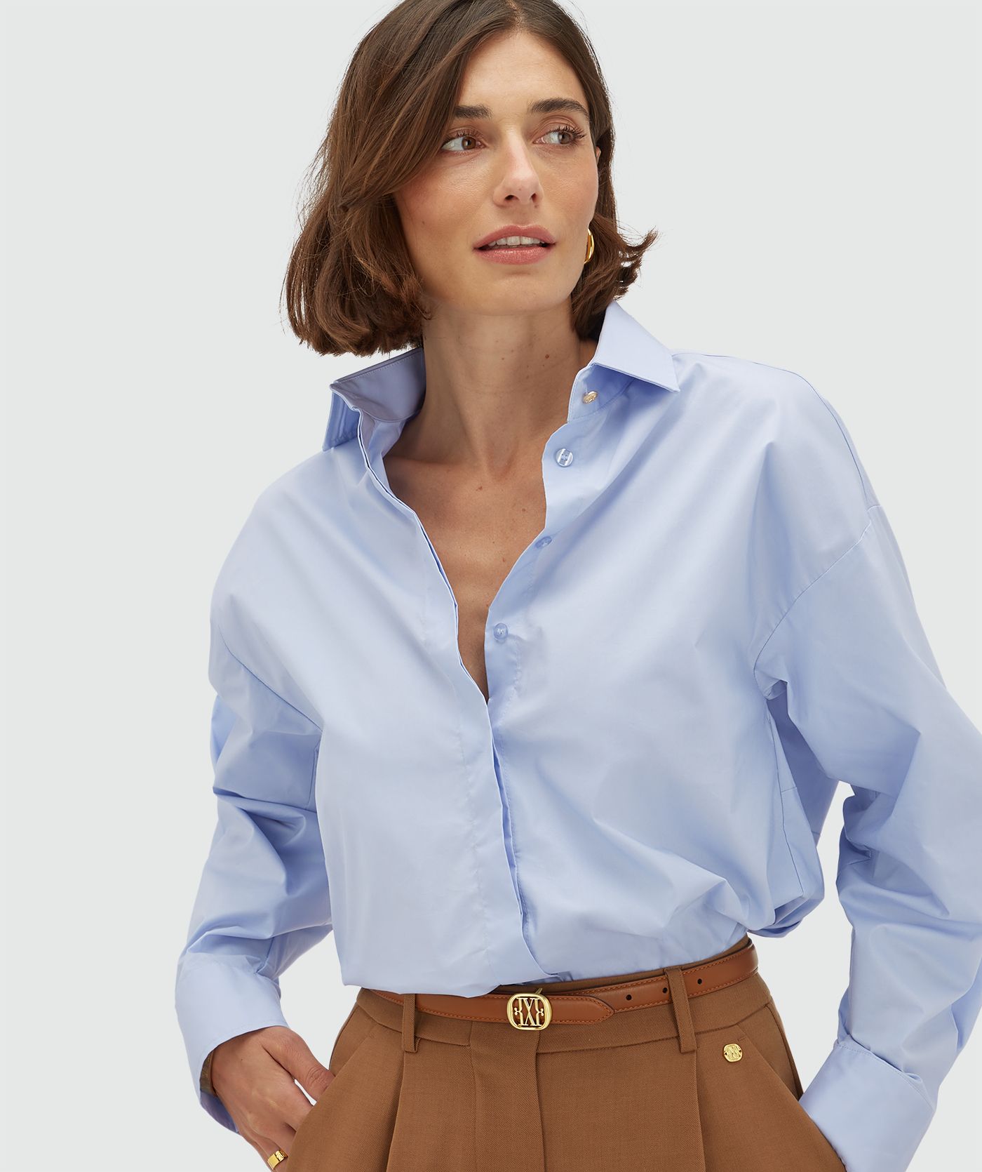 Model draagt een oversized licht blauwe blouse met strikdetail aan de achterzijde. 