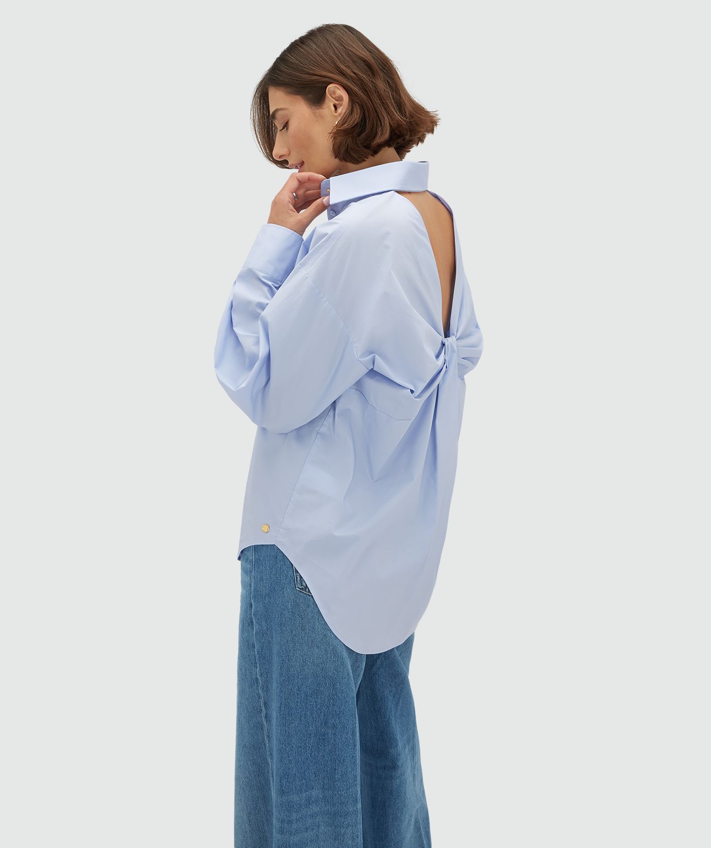 Zijaanzicht van een model in een oversized licht blauwe blouse met strikdetail aan de achterzijde. 