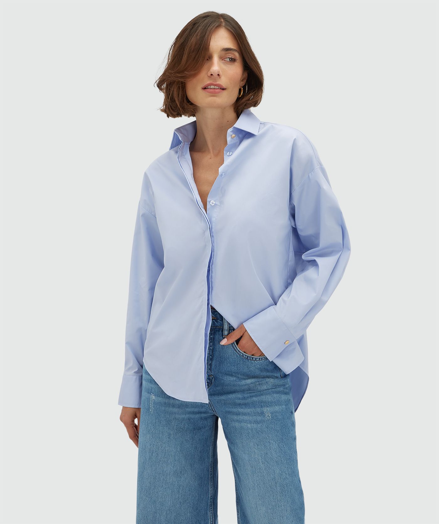 Model draagt een oversized licht blauwe blouse met strikdetail aan de achterzijde. 