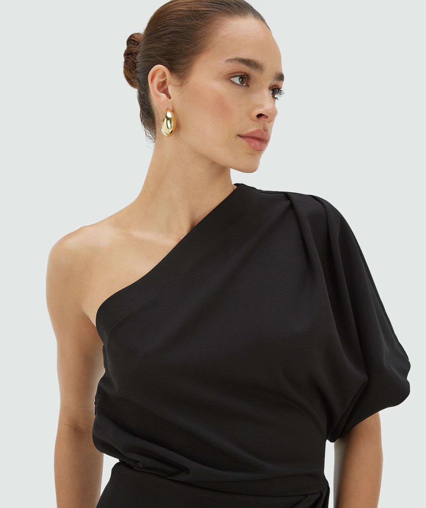 Model draagt een aangesloten zwarte one shoulder jurk met asymmetrische halslijn - JOSH V