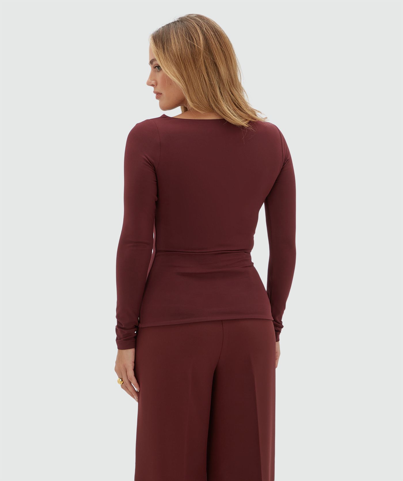 Achteraanzicht van een model in een donkerrode top gecombineerd met een donkerrode pantalon.