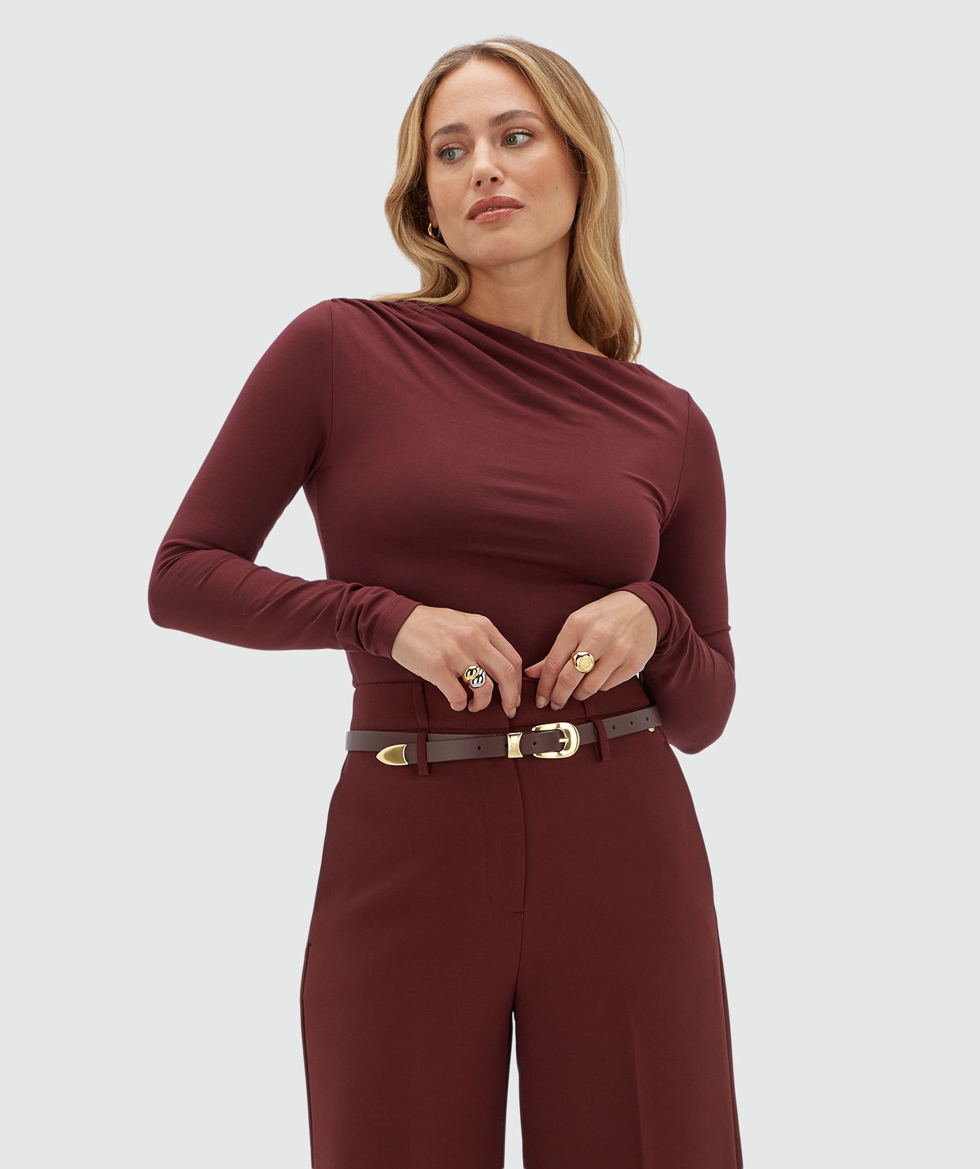 Model draagt een donkerrode top met een a-symmetrische hals lijn gecombineerd met een donkerrode pantalon.