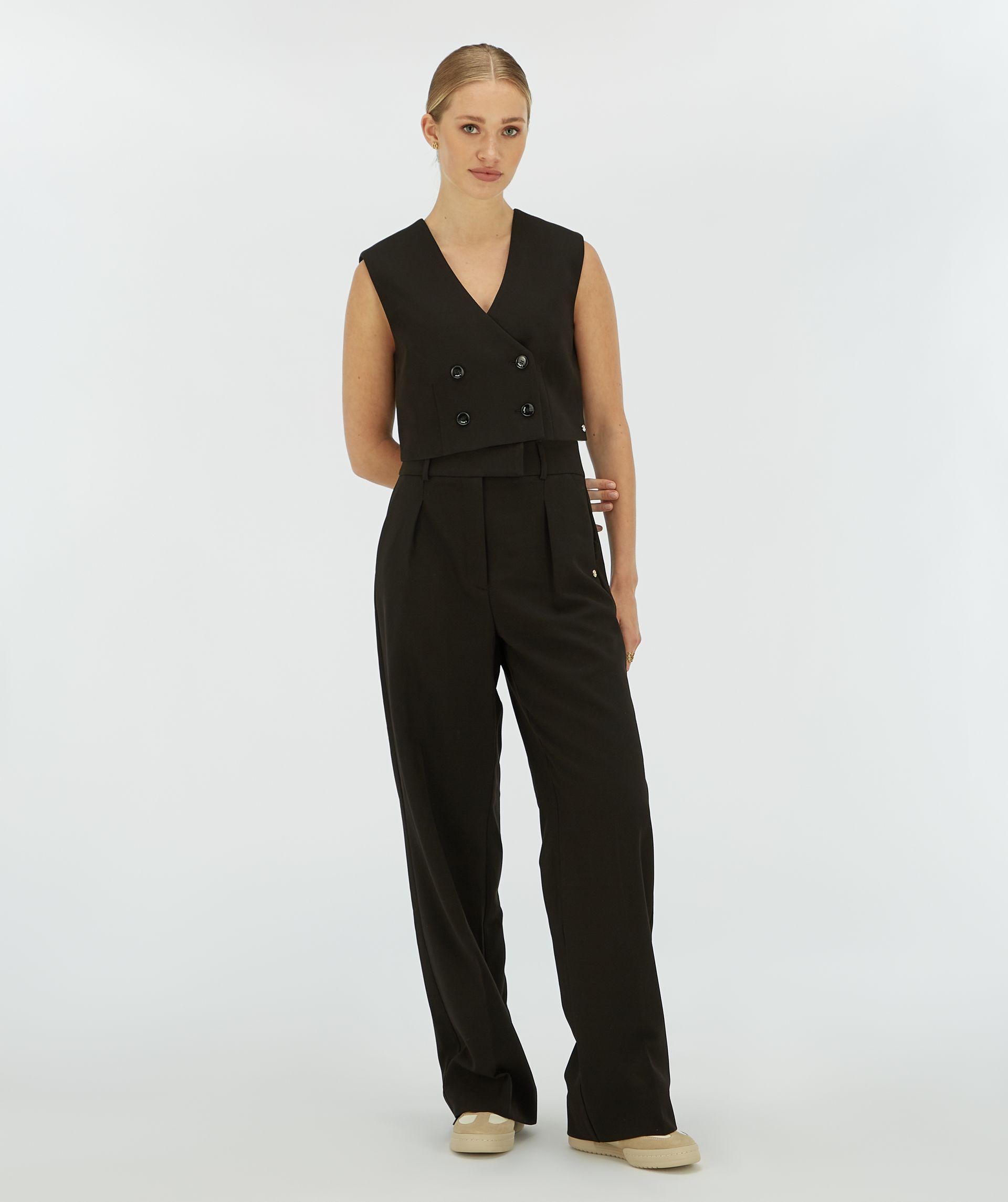 Model draagt een zwart cropped gilet met vier knopen aan de voorkant.