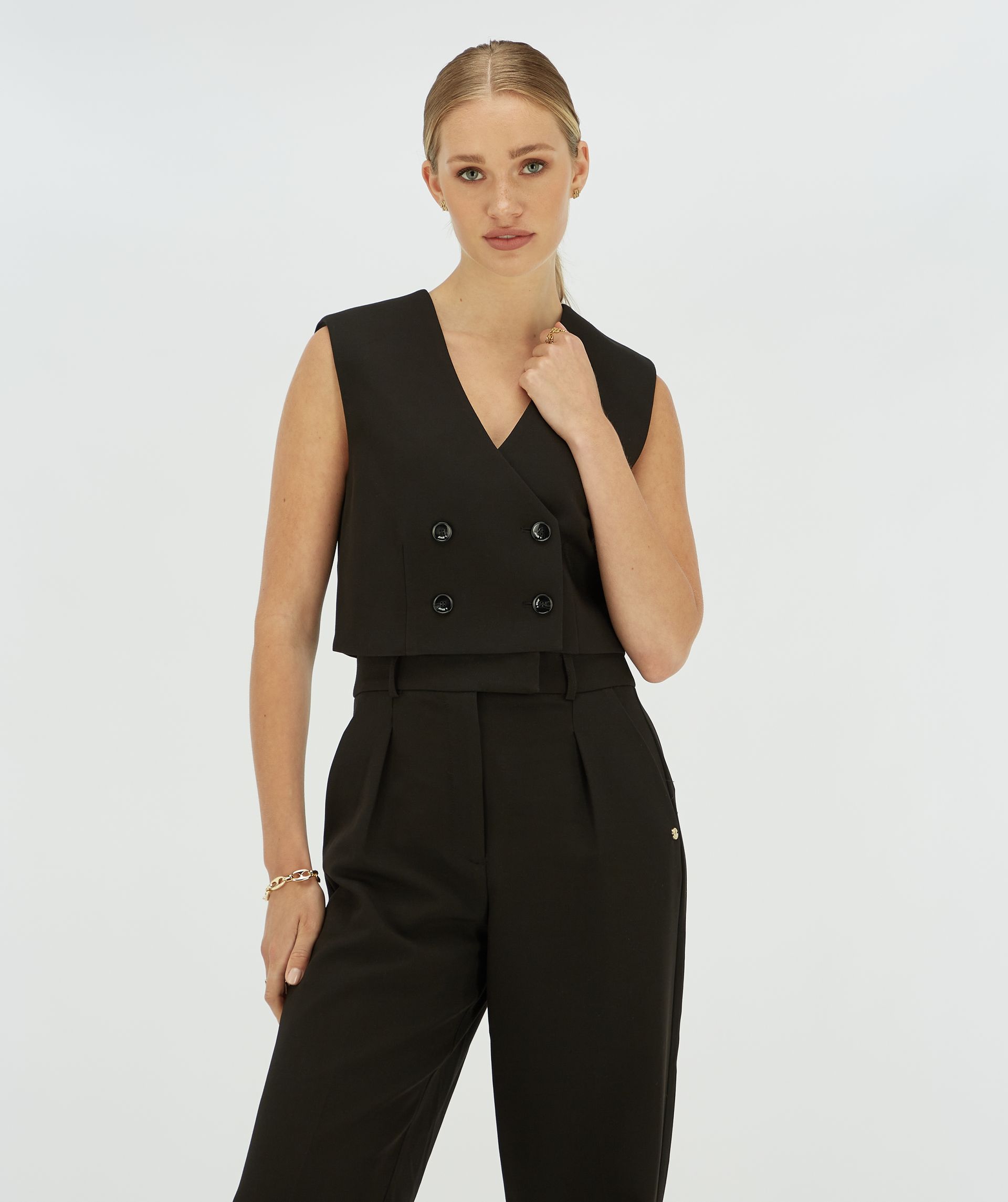 Model draagt een zwart cropped gilet met vier knopen aan de voorkant.