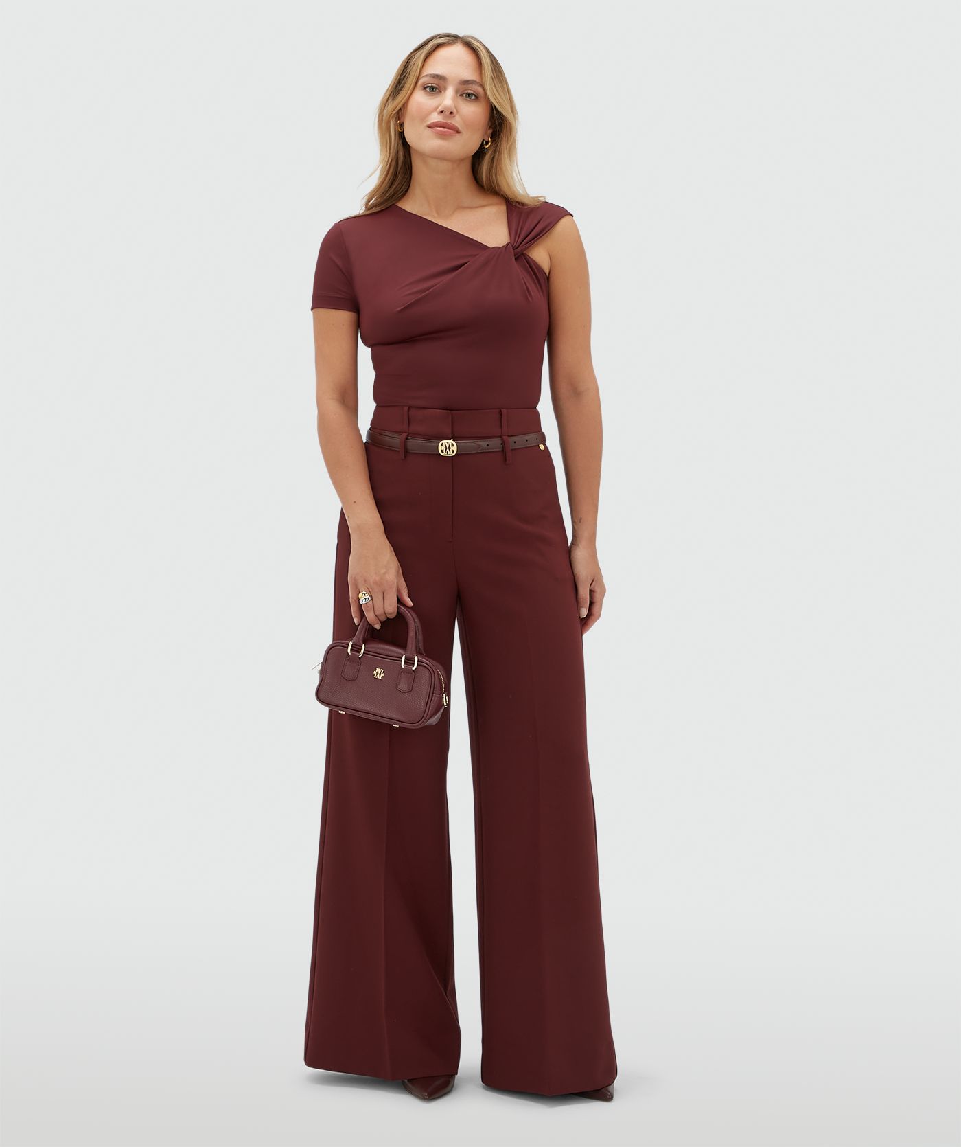 Model draagt een donkerrode body met een knoop detail op de borst gecombineerd met donkerrode pantalon.