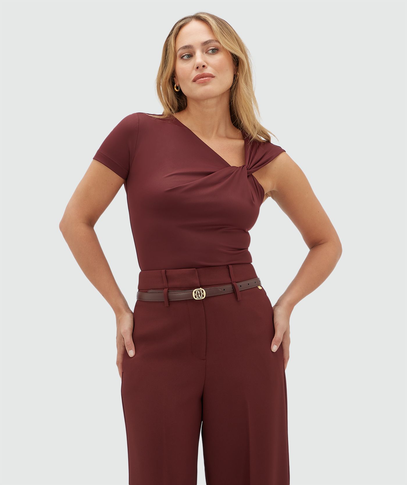 Model draagt een donkerrode body met een knoop detail op de borst gecombineerd met donkerrode pantalon.