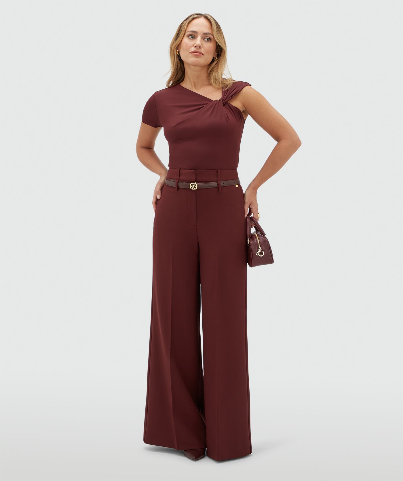 Model draagt een donkerrode body met een knoop detail op de borst gecombineerd met donkerrode pantalon.