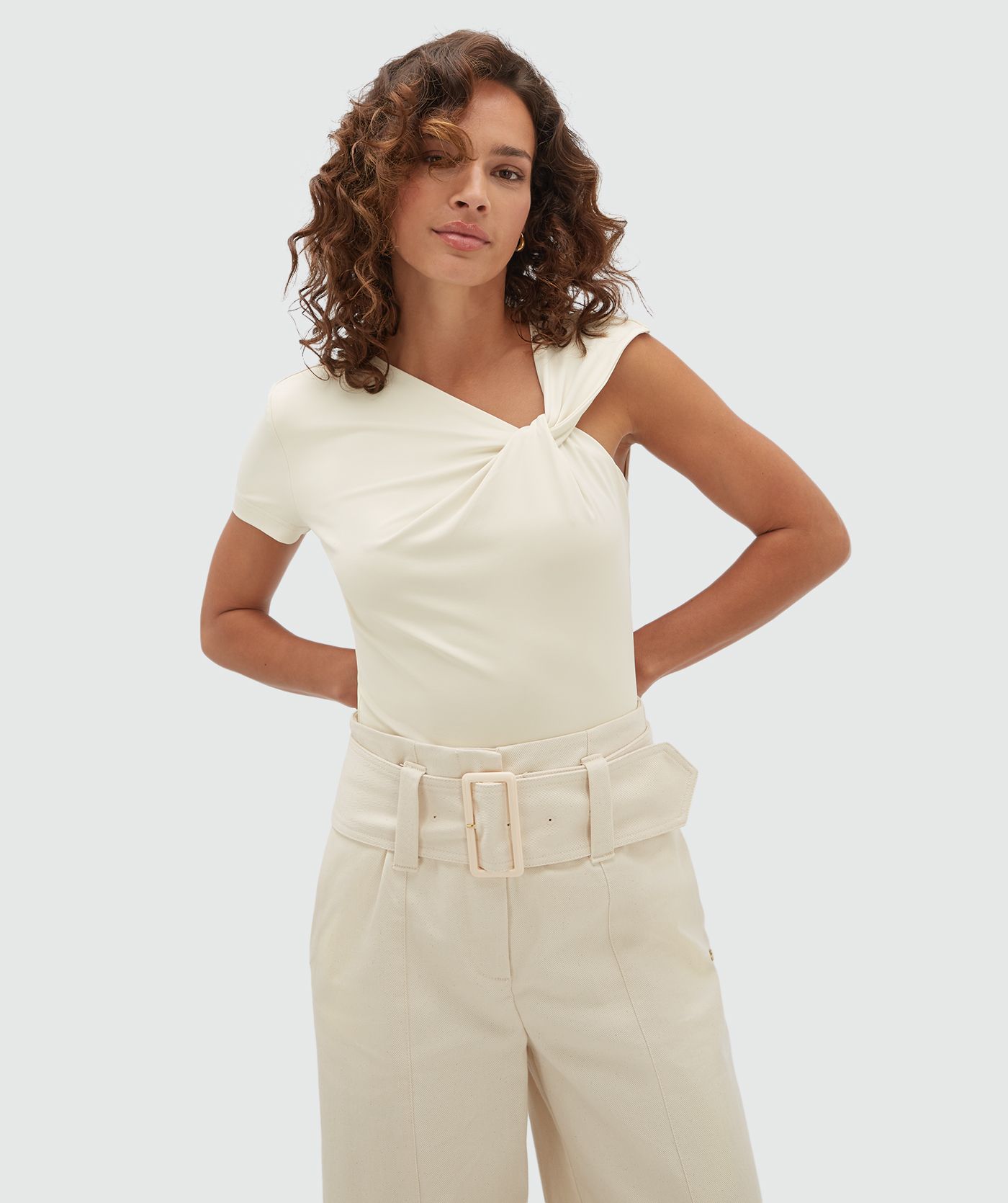 Model draagt een gebroken witte body met een knoop detail bij de linker arm.