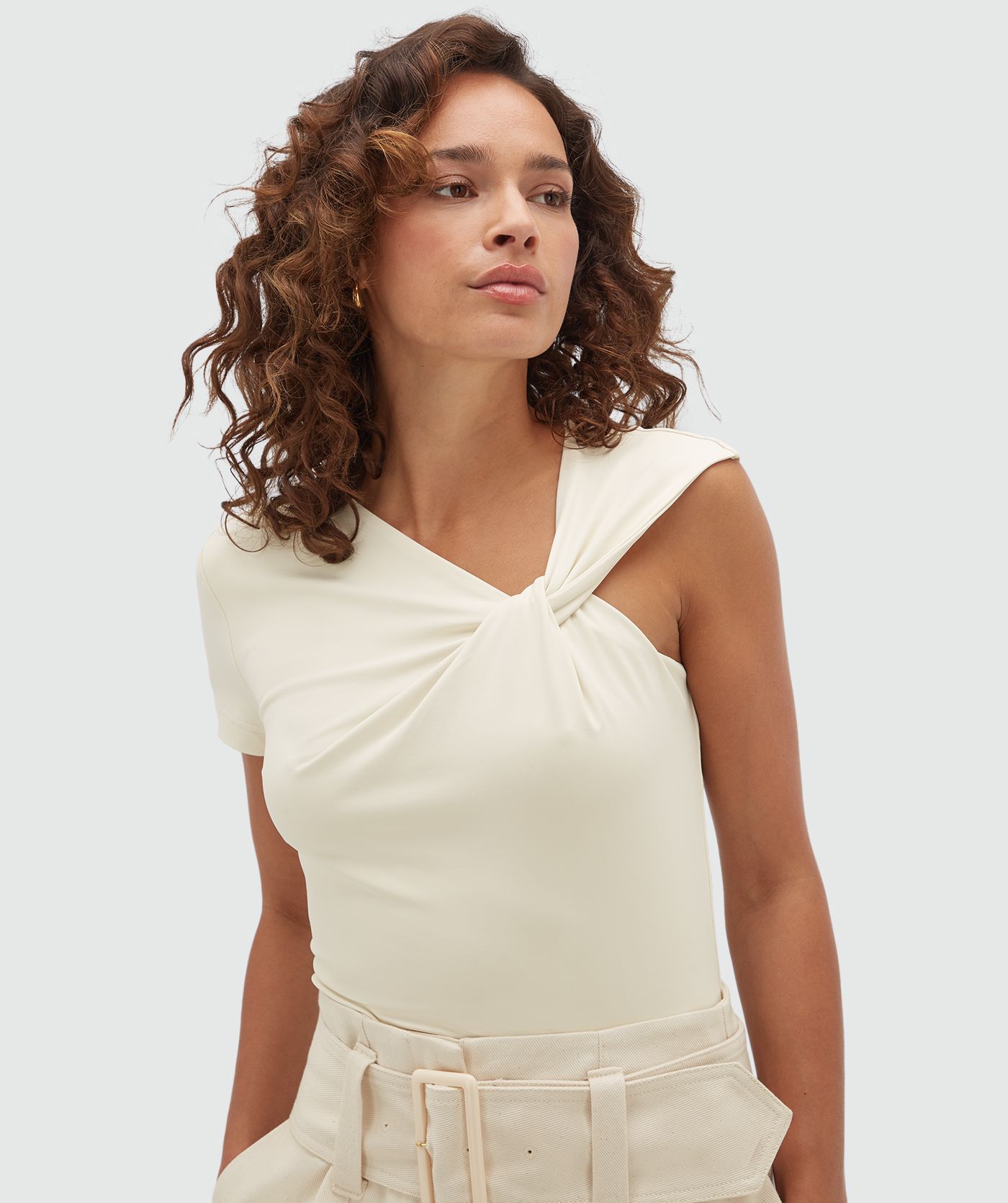 Model draagt een gebroken witte body met een knoop detail bij de linker arm.