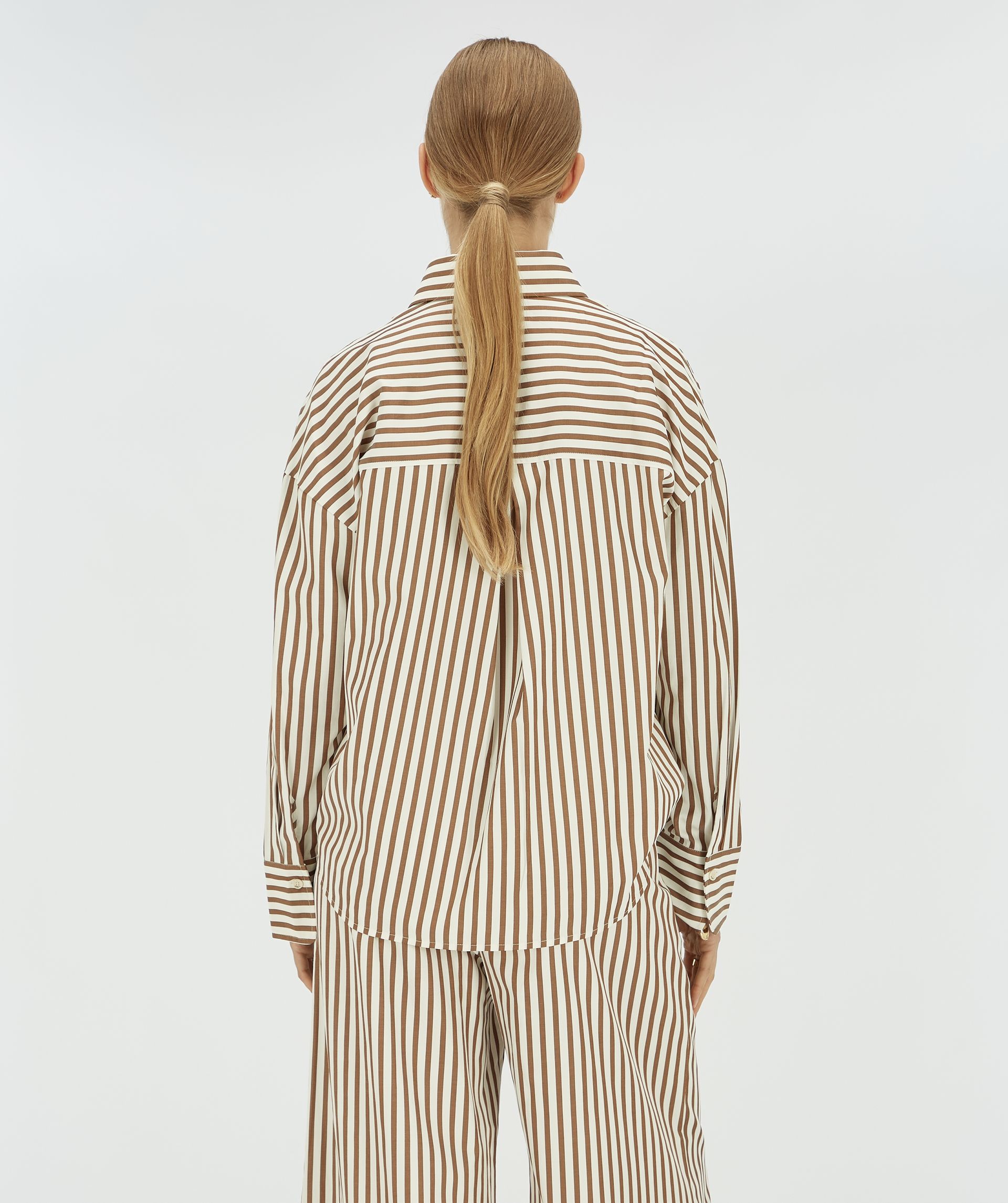 Achteraanzicht van een model in een wit met donkerbruin gestreepte blouse. 