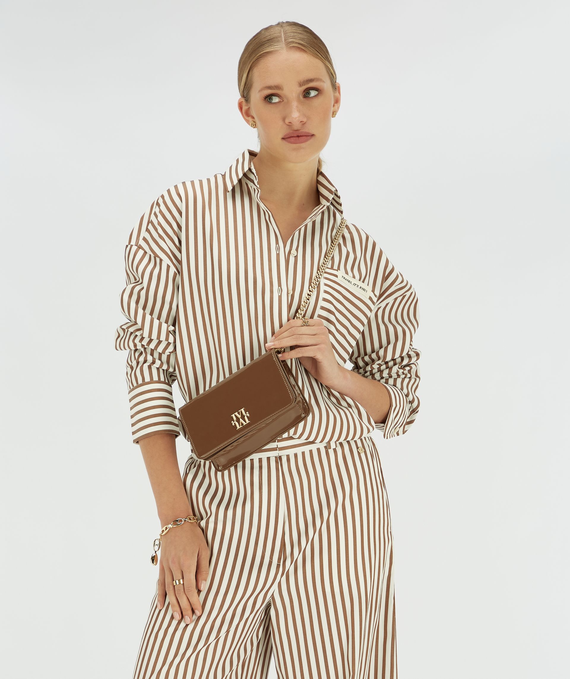 Model draagt een wit met donkerbruin gestreepte blouse. 
