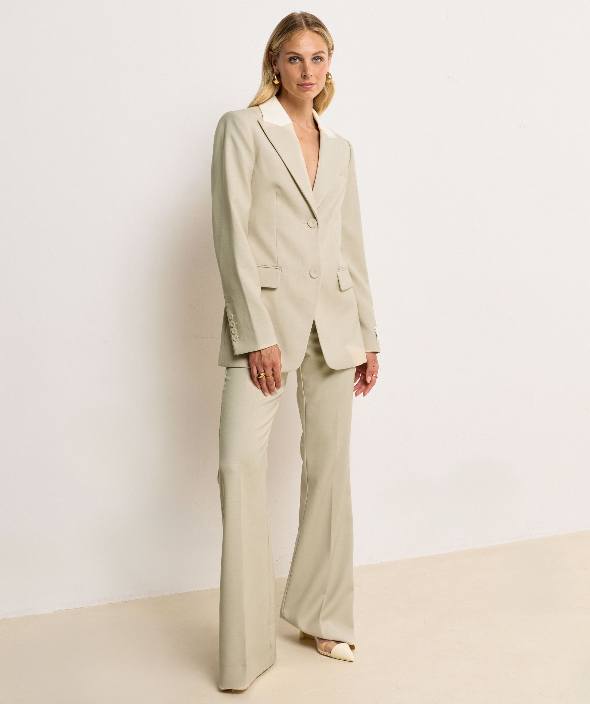 Model draagt in een high rise flared pantalon met een dubbele band in de kleur Ecru Melange, hierbij is de bovenste band van de pantalon in Ecru en de rest van de broek in de kleur Melange