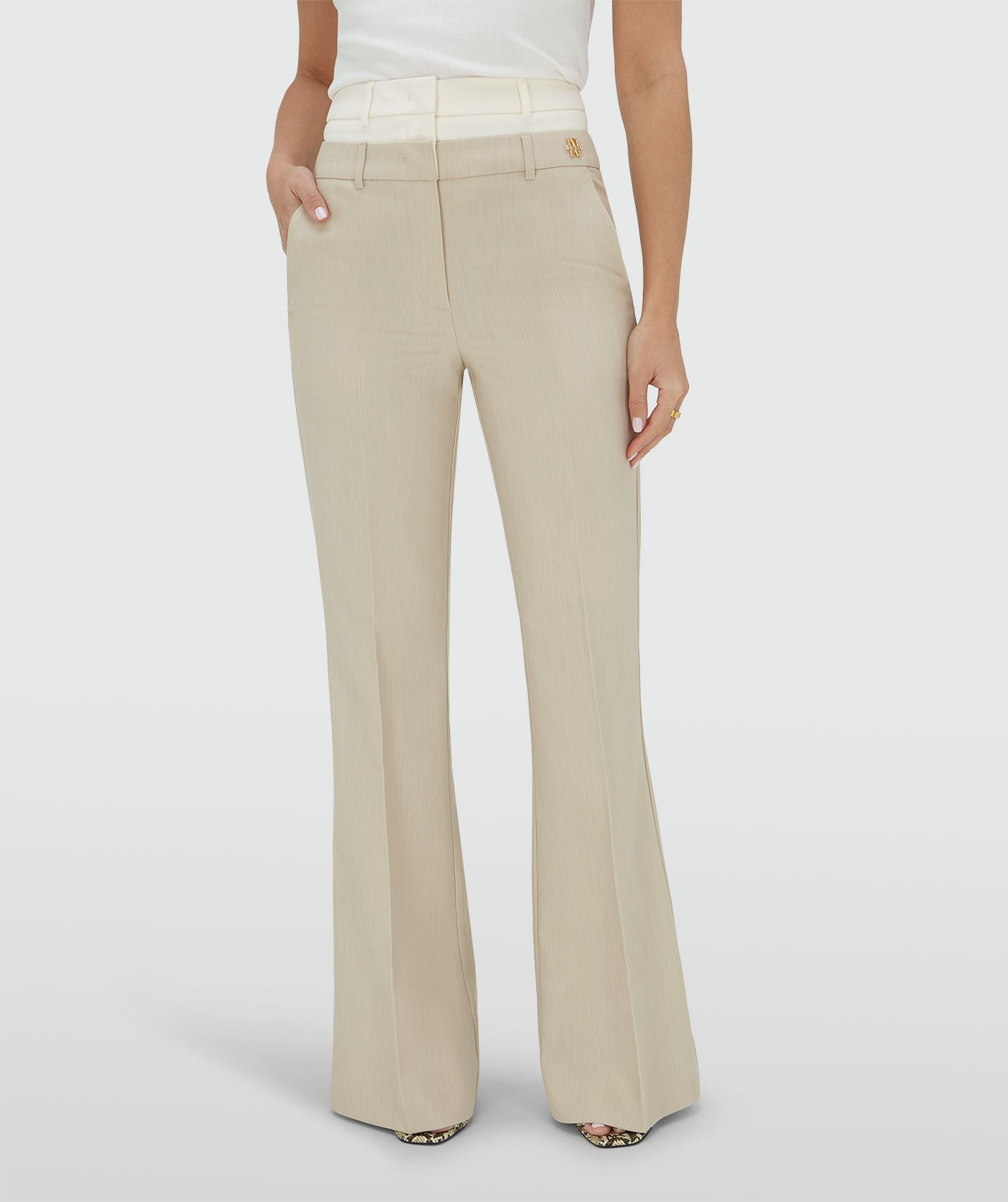 Ingezoomd beeld waarin het model een high rise flared pantalon draagt met een dubbele band in de kleur Ecru Melange, hierbij is de bovenste band van de pantalon in Ecru en de rest van de broek in de kleur Melange