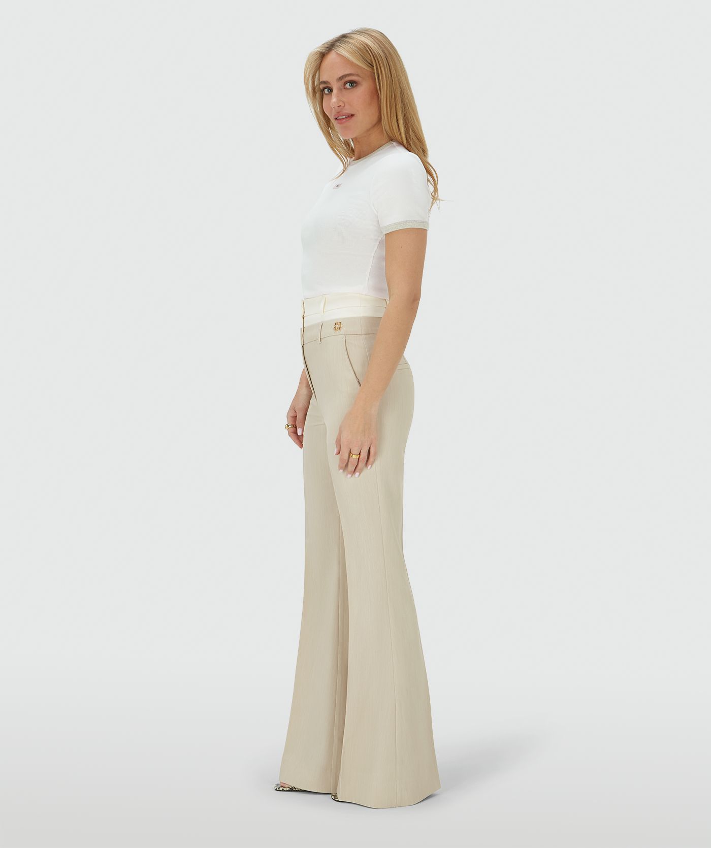 Zijaanzicht van een model in een high rise flared pantalon met een dubbele band in de kleur Ecru Melange, hierbij is de bovenste band van de pantalon in Ecru en de rest van de broek in de kleur Melange