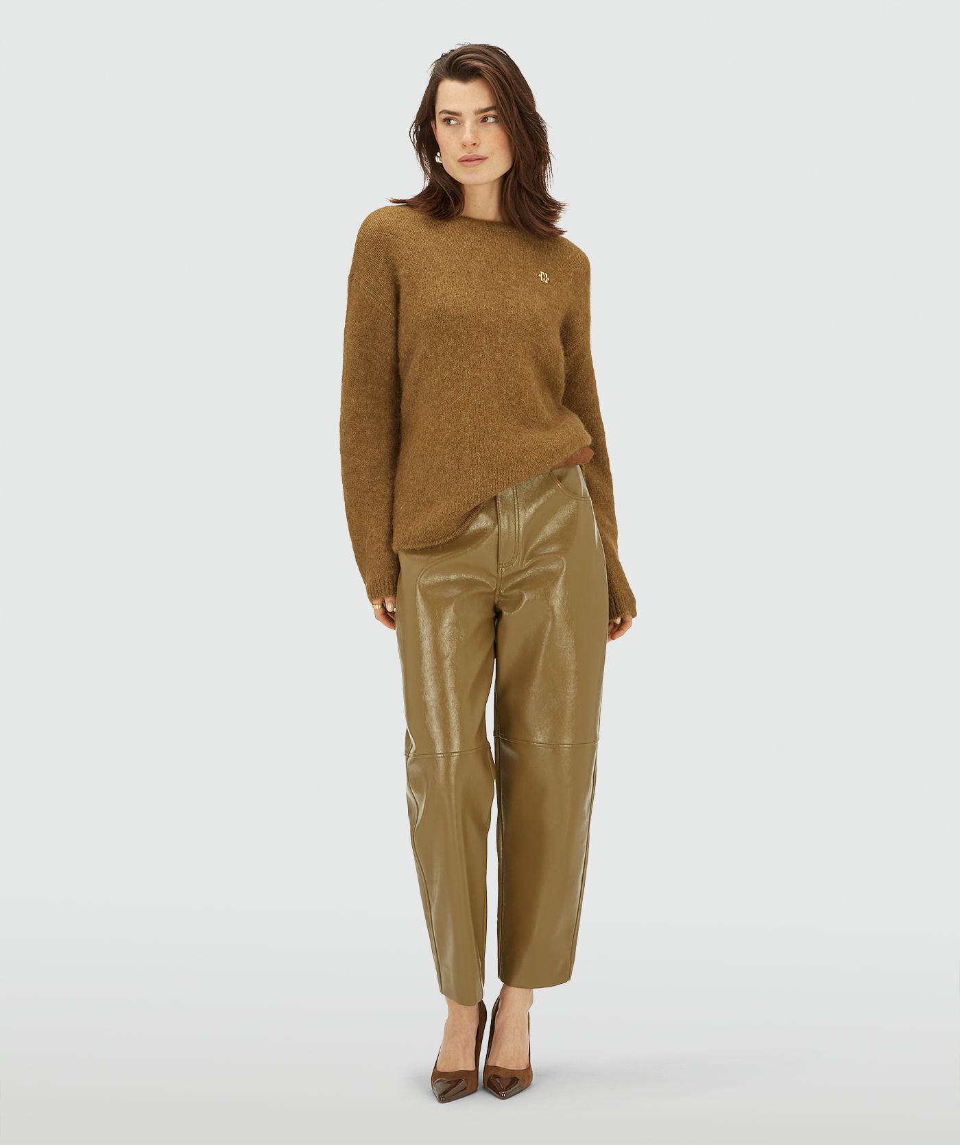 Model draagt een Olive Green Melange trui met ronde hals en lange mouwen, afgewerkt met een klein goudkleurig logo op de borst.