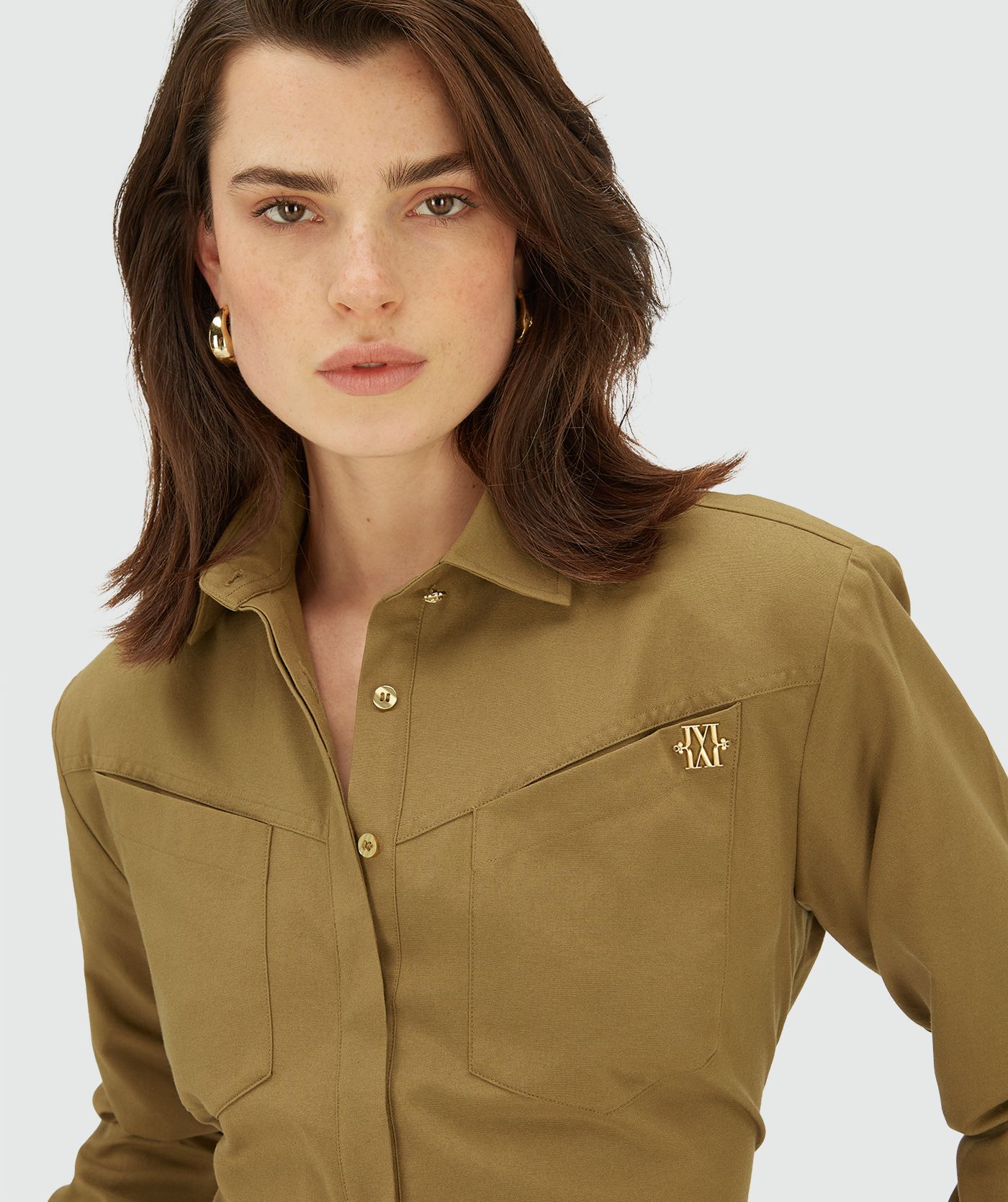 Model draagt een Olive Green blouse met lange mouwen, knoopsluiting en twee borstzakken. Het overhemd heeft een getailleerde pasvorm en een subtiel goudkleurig JOSH V-logo op de borst